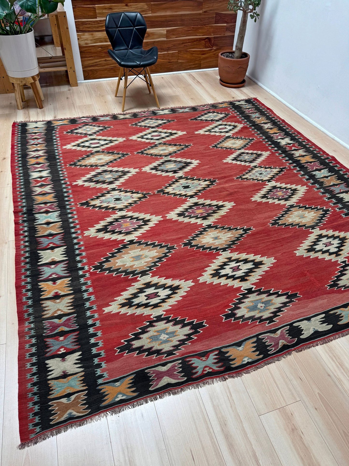 Decorative rug with geometric pattern on a wooden floor. Vintage handmade Pirot kilim rug from the Balkans 8x8 ft with Sofra diamond design in madder red, ivory, and indigo hues – tribal wool flatweave, available in Burlingmade, SF Bay Area with free shipping.