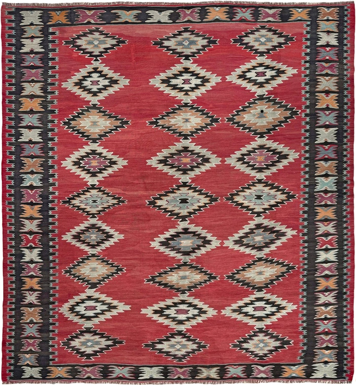 Decorative rug with geometric pattern on a wooden floor. Vintage handmade Pirot kilim rug from the Balkans 8x8 ft with Sofra diamond design in madder red, ivory, and indigo hues – tribal wool flatweave, available in Burlingmade, SF Bay Area with free shipping.