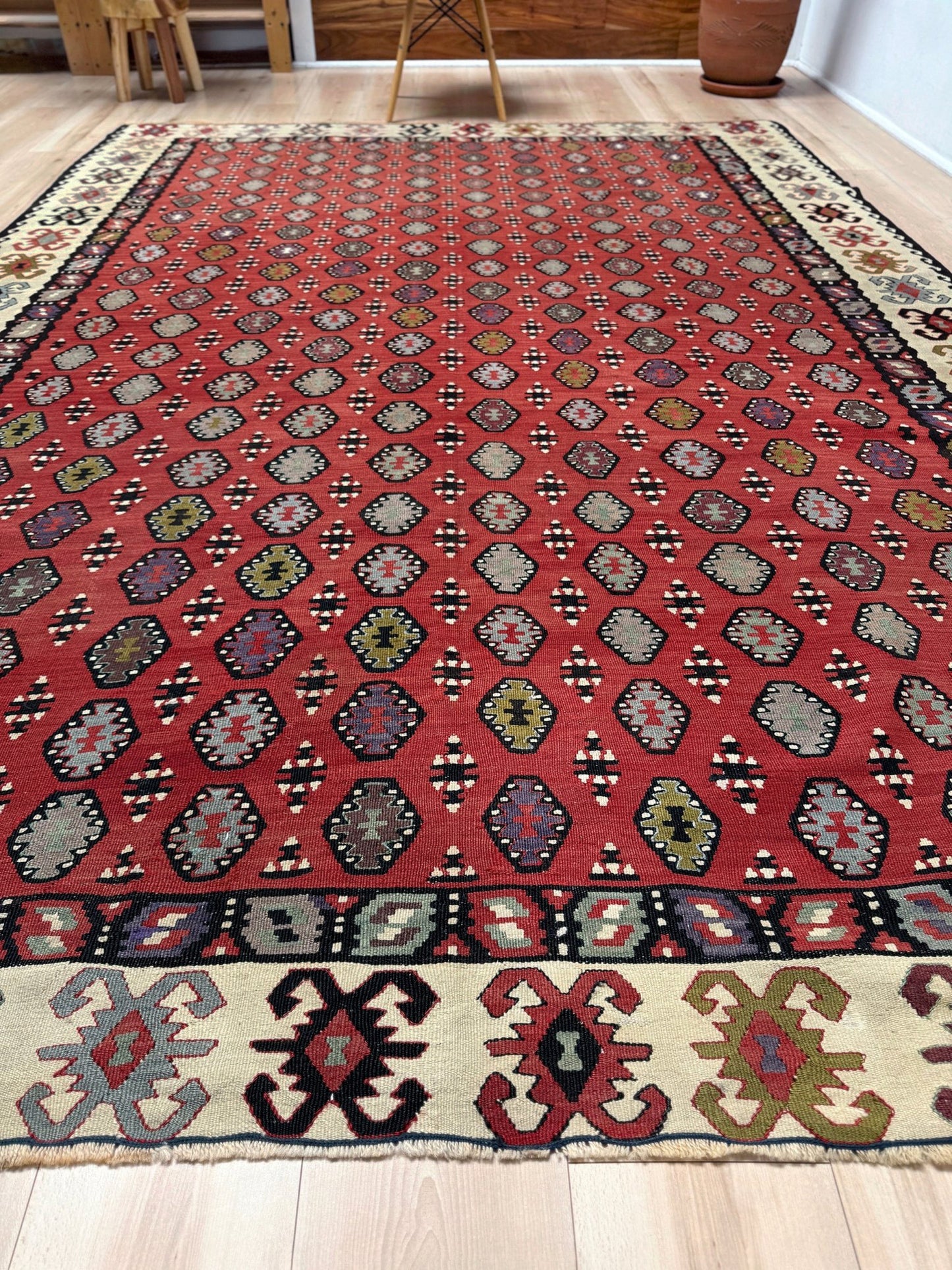 Decorative rug with intricate pattern on a red background. Vintage Pirot kilim with warm madder red field and repeating geometric medallions, handwoven wool flatweave rug with ivory border, approx. 7x10.