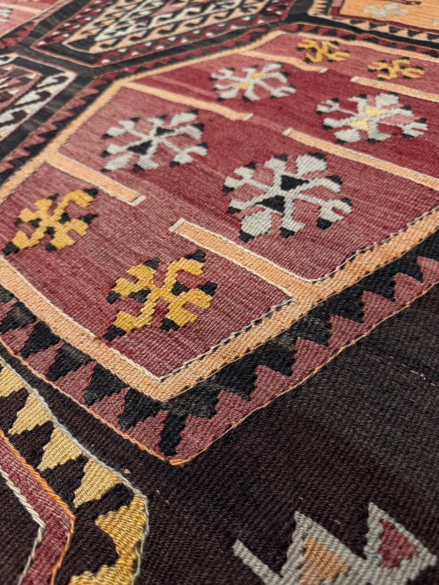 Close-up of a patterned rug with geometric designs. Vintage Sarkisla Turkish kilim rug 6x9 with deep brown field and geometric medallions in madder red, camel, and ivory tones — handmade Anatolian flatweave carpet