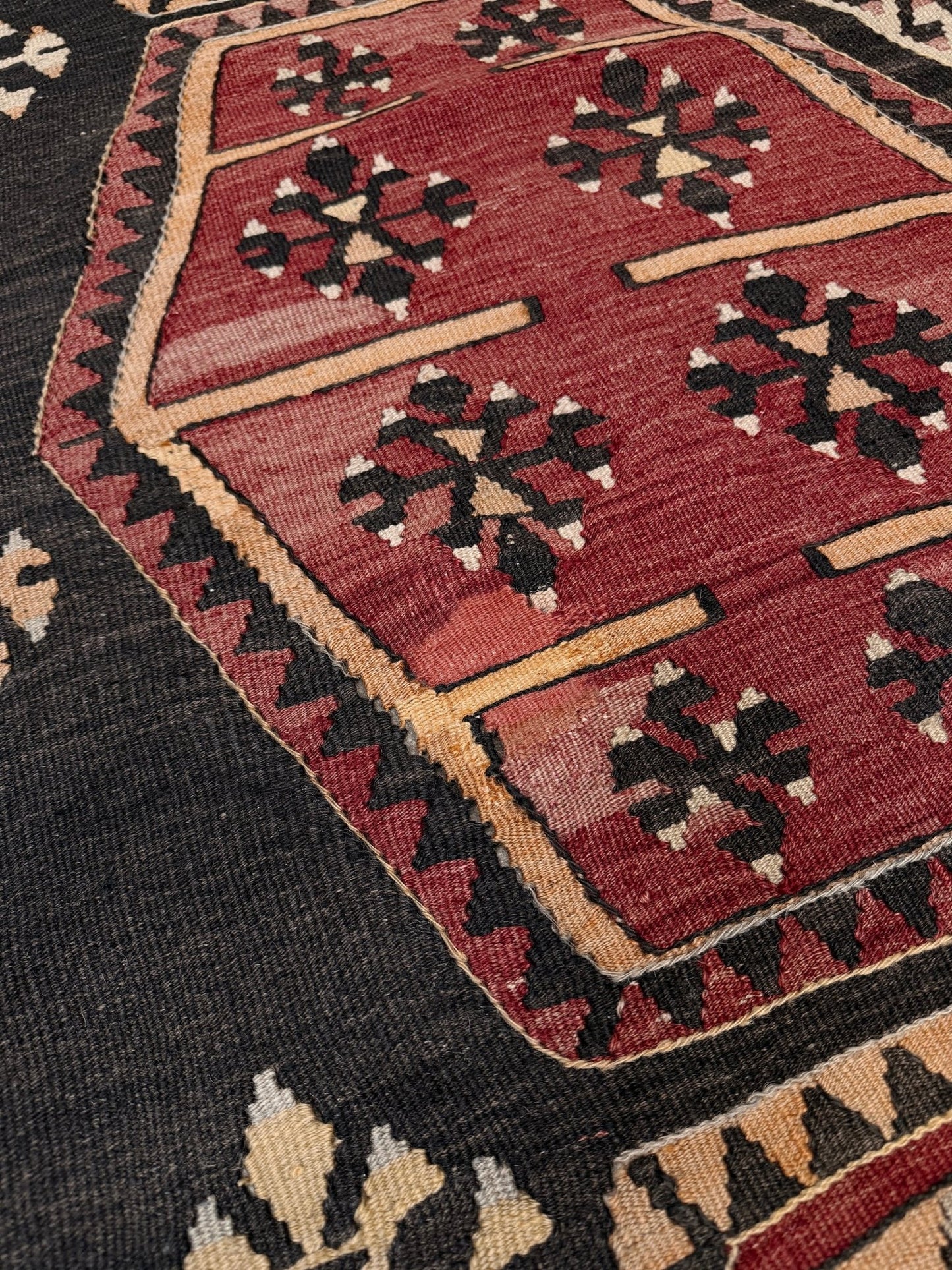 Close-up of a patterned rug with red, black, and beige colors. Vintage Sarkisla Turkish kilim rug 6x9 with deep brown field and geometric medallions in madder red, camel, and ivory tones — handmade Anatolian flatweave carpet