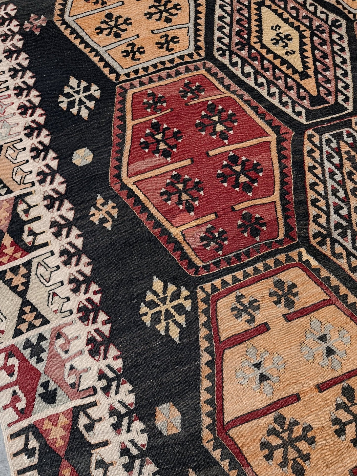 Close-up of a patterned rug with geometric designs in red, black, and beige. Vintage Sarkisla Turkish kilim rug 6x9 with deep brown field and geometric medallions in madder red, camel, and ivory tones — handmade Anatolian flatweave carpet