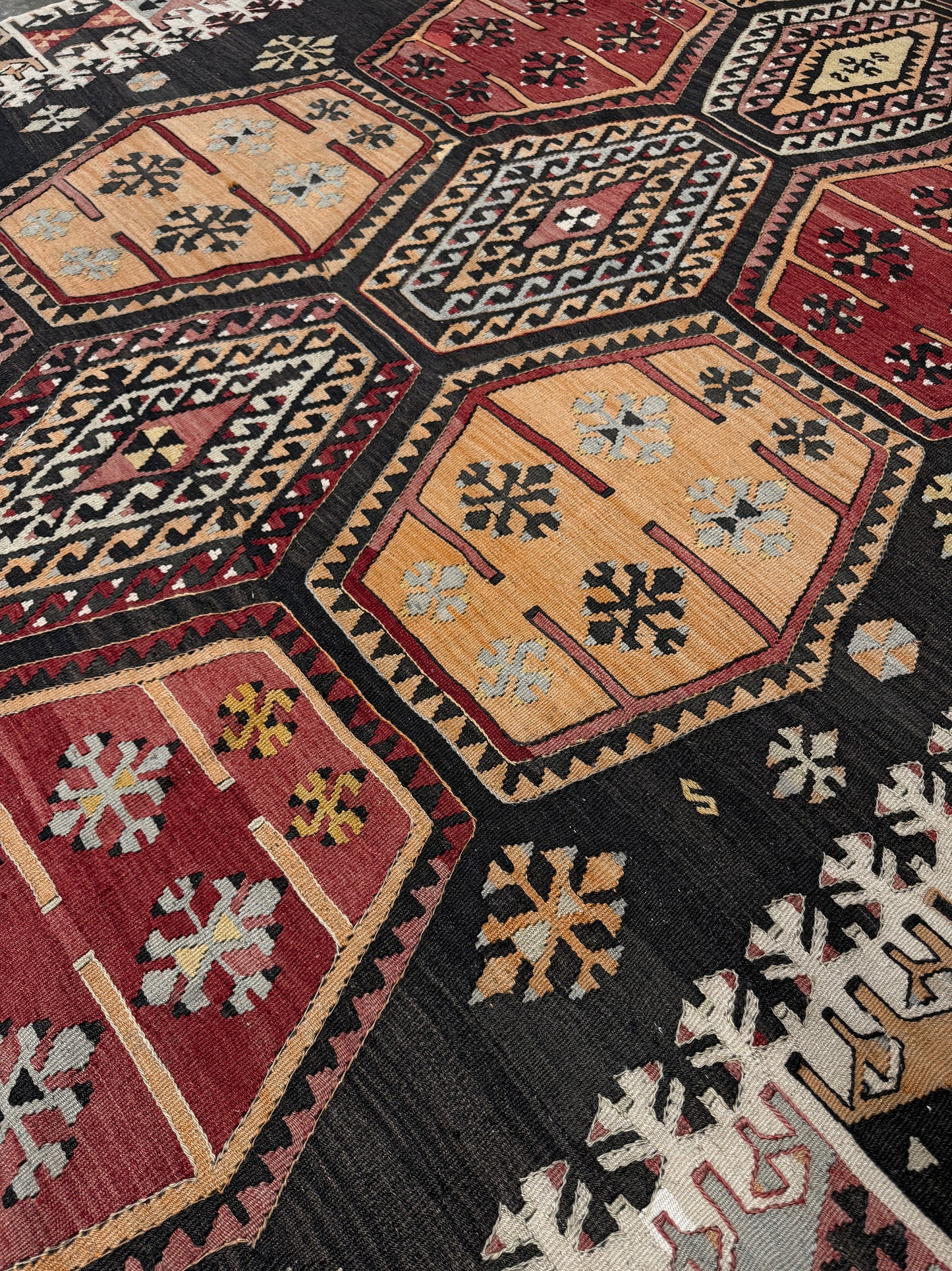 Close-up of a patterned rug with geometric designs in red, black, and beige. Vintage Sarkisla Turkish kilim rug 6x9 with deep brown field and geometric medallions in madder red, camel, and ivory tones — handmade Anatolian flatweave carpet