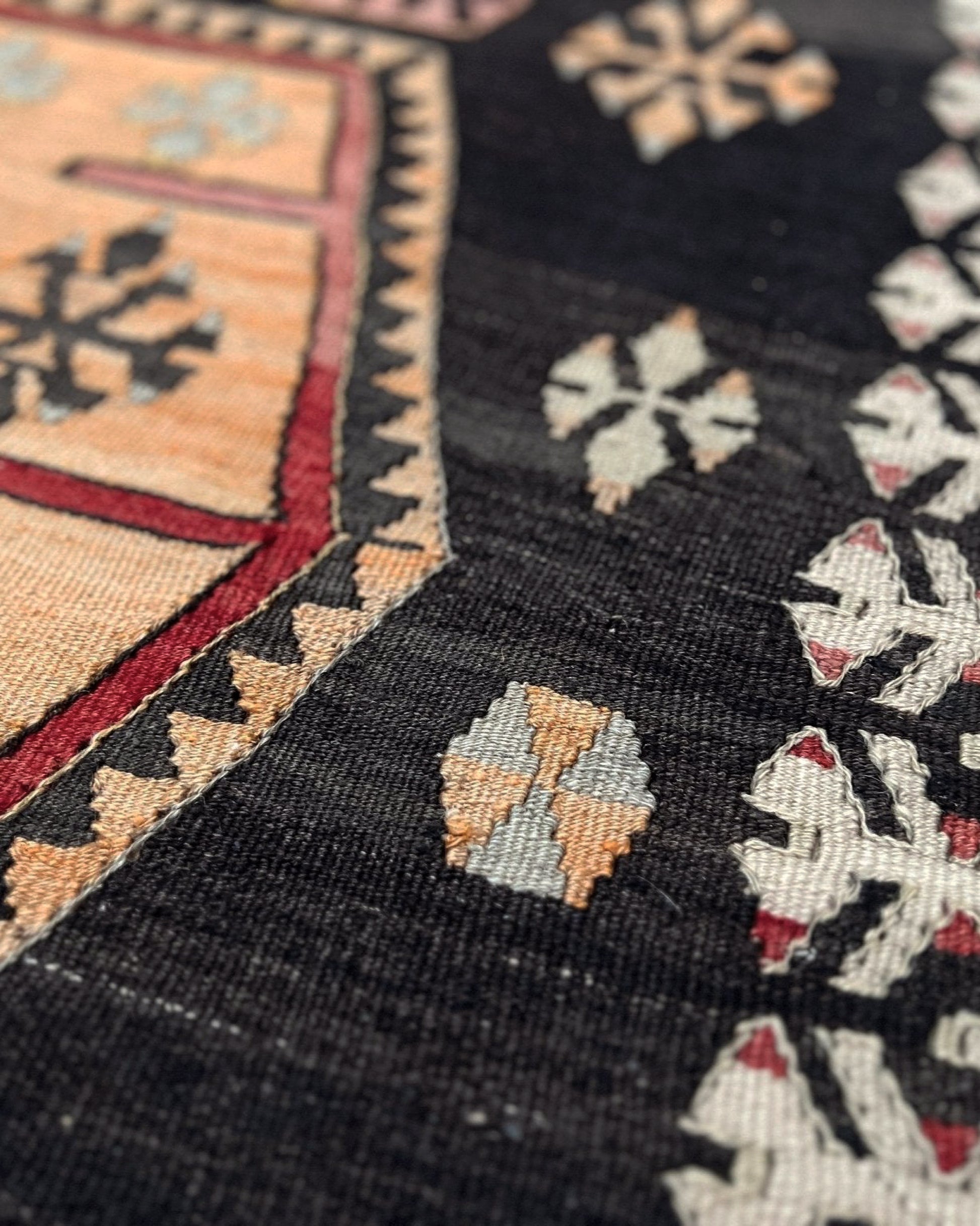 Close-up of a patterned fabric with geometric designs on a black background. Vintage Sarkisla Turkish kilim rug 6x9 with deep brown field and geometric medallions in madder red, camel, and ivory tones — handmade Anatolian flatweave carpet