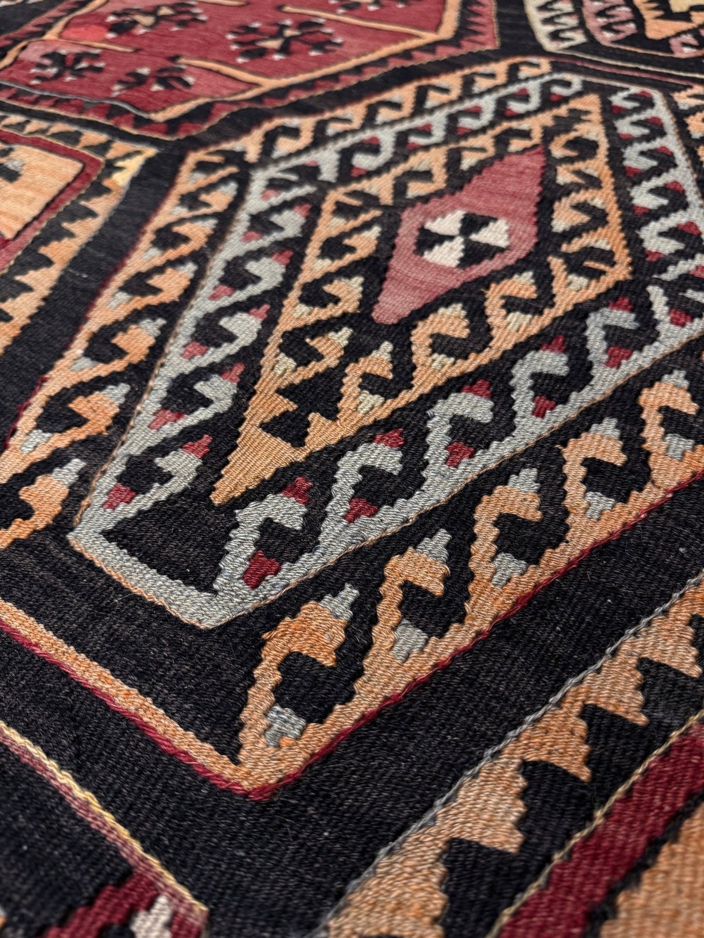 Close-up of a patterned rug with geometric design. Vintage Sarkisla Turkish kilim rug 6x9 with deep brown field and geometric medallions in madder red, camel, and ivory tones — handmade Anatolian flatweave carpet