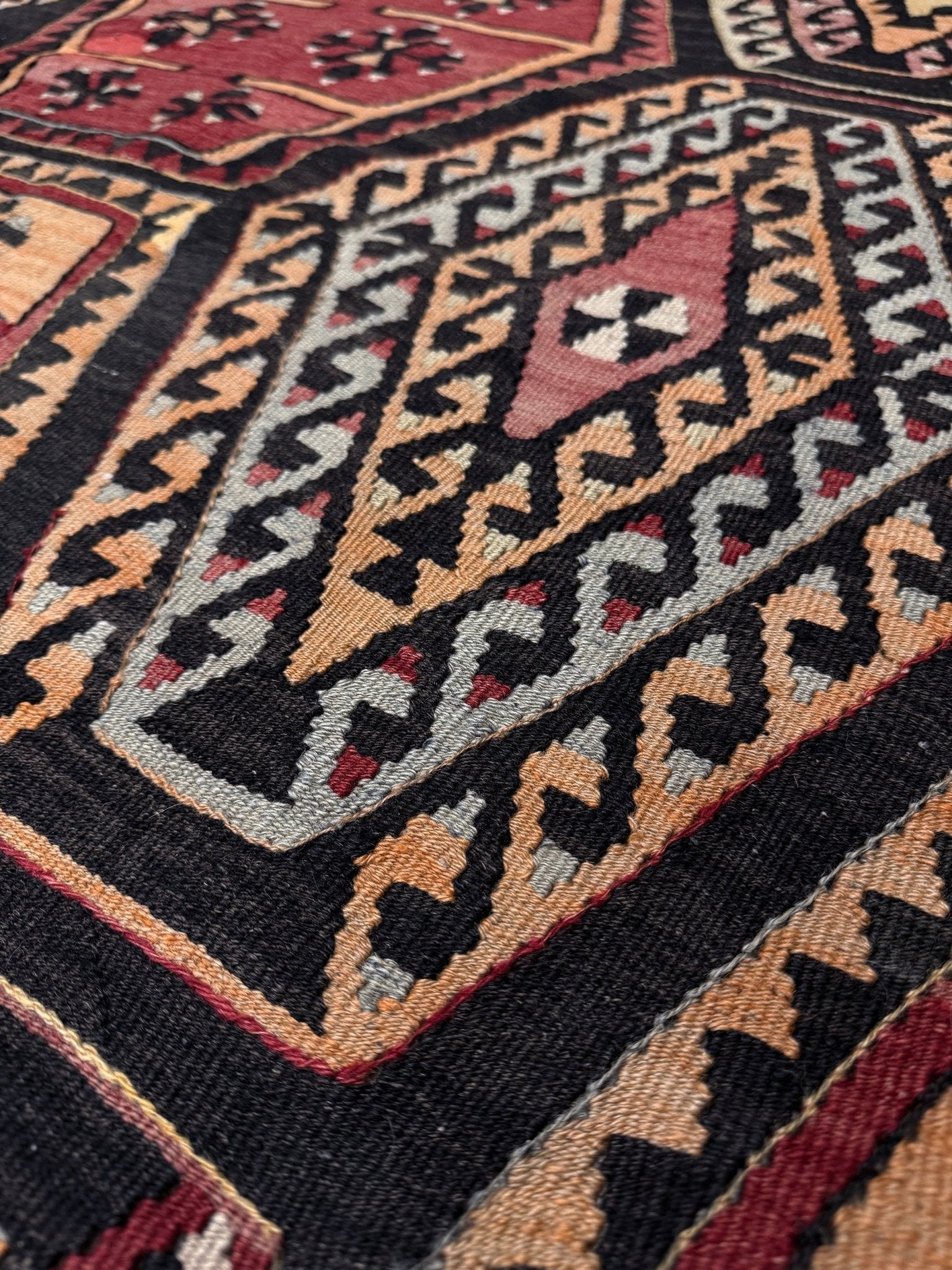 Close-up of a patterned rug with geometric design. Vintage Sarkisla Turkish kilim rug 6x9 with deep brown field and geometric medallions in madder red, camel, and ivory tones — handmade Anatolian flatweave carpet