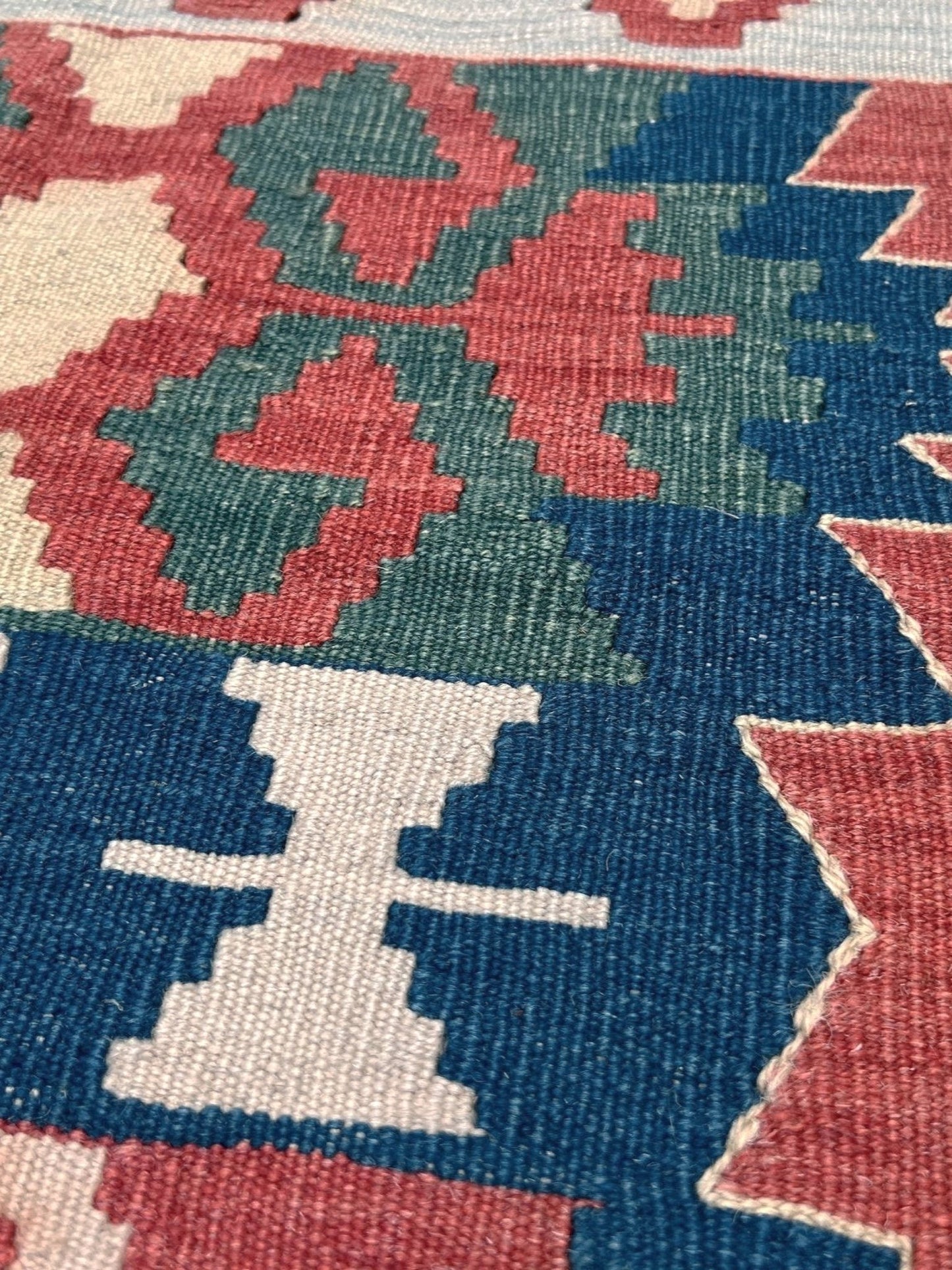 Close-up of a patterned rug with geometric design. Woven turkish kilim rug with geometric pattern featuring red, blue, and beige colors. 