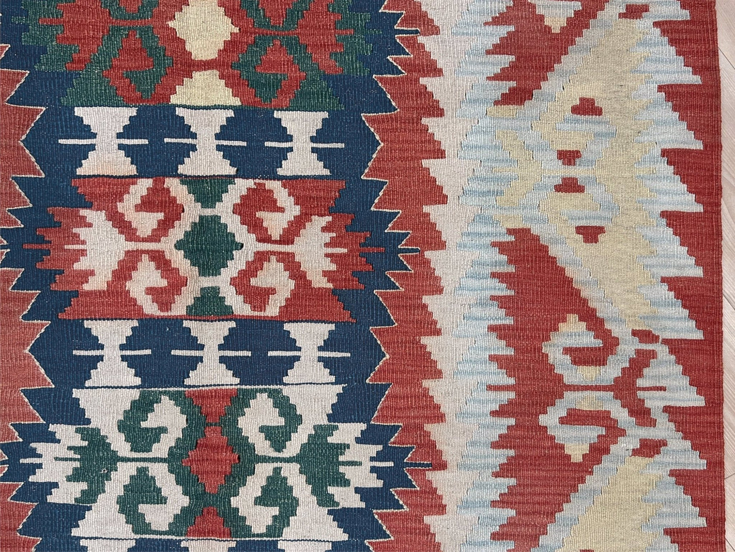 Woven turkish kilim rug with geometric pattern featuring red, blue, and beige colors. 