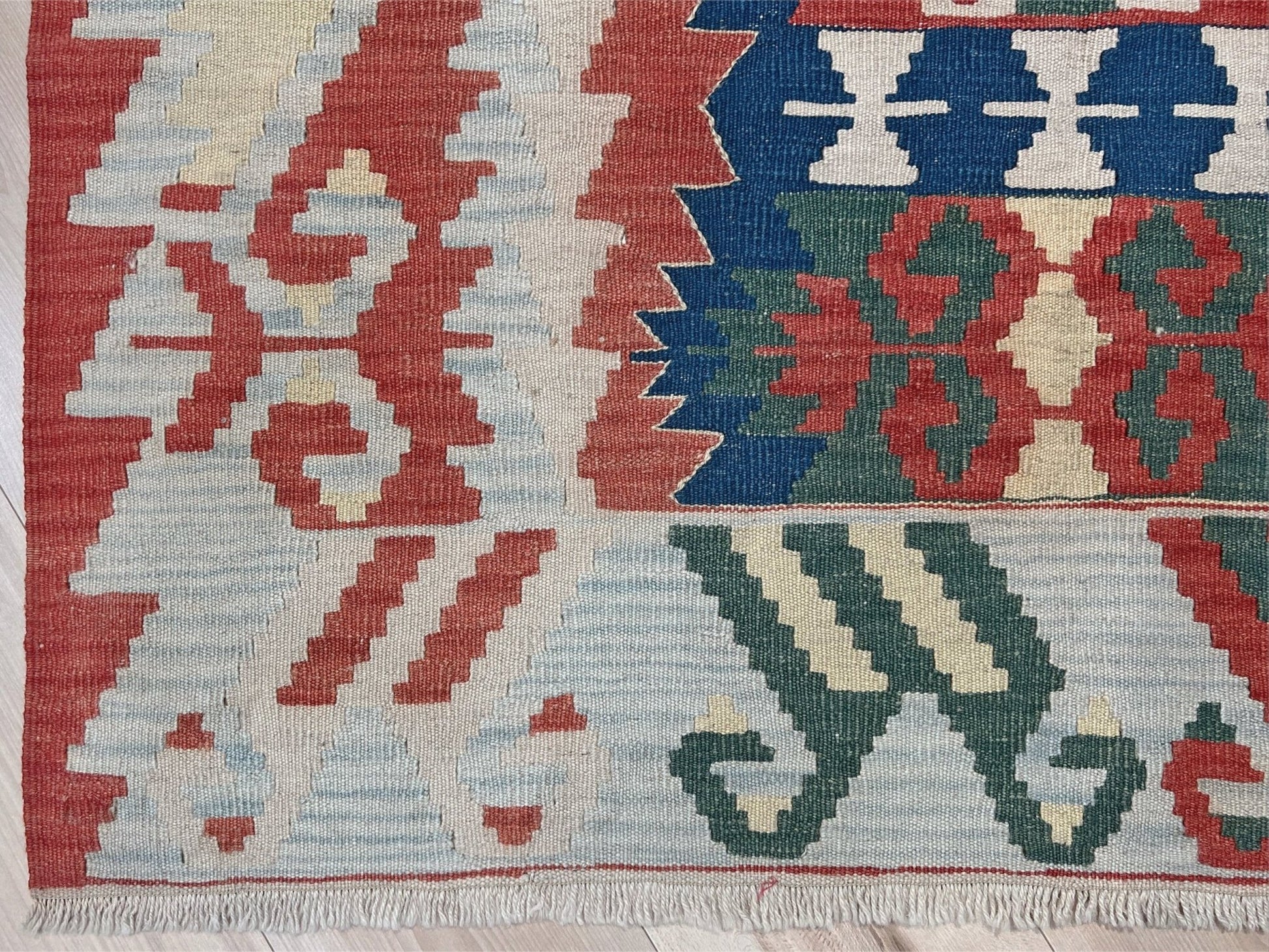 Woven turkish kilim rug with geometric pattern featuring red, blue, and beige colors. 