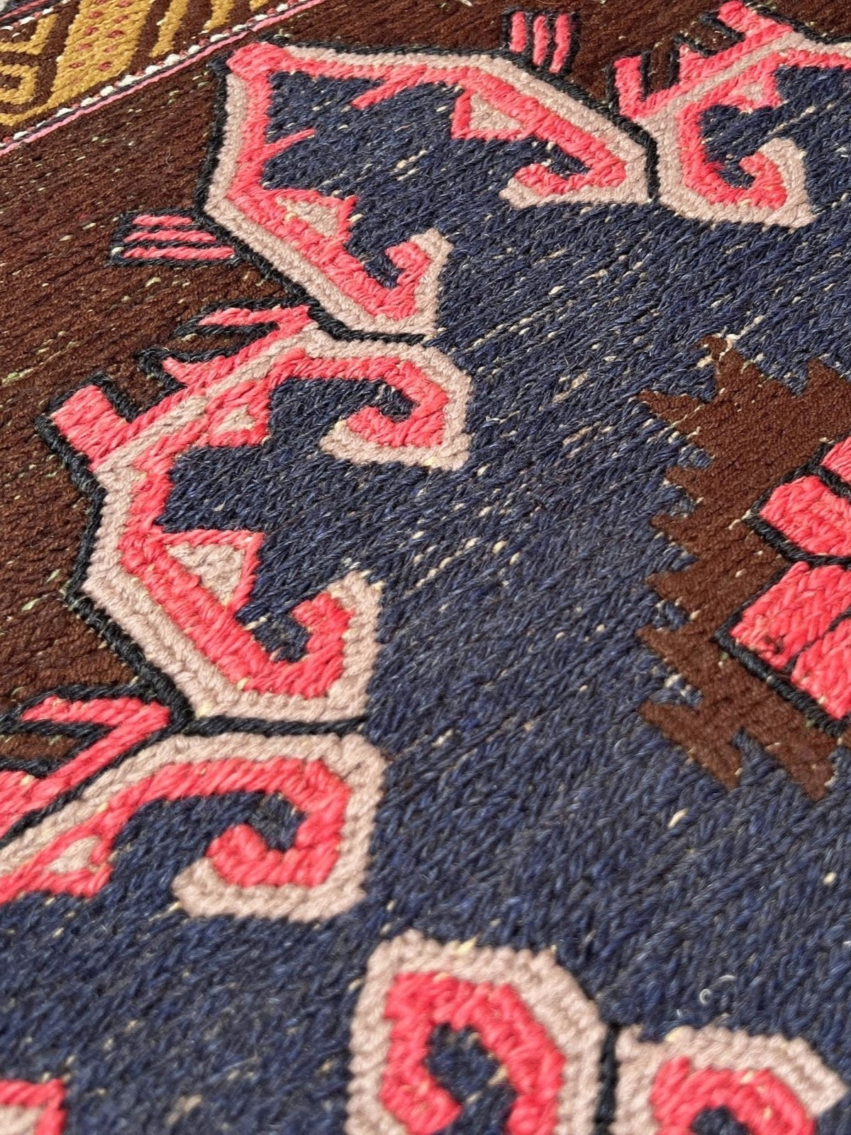 Close-up of a woven rug with a dark navy blue field, brown geometric motifs, and coral pink accents outlined in cream.