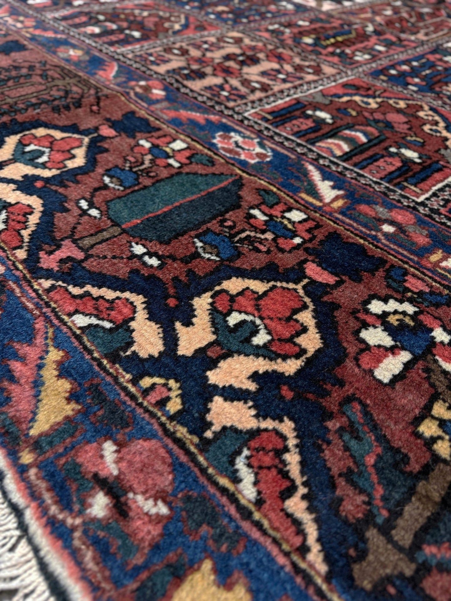 Close-up of a patterned rug with intricate designs. 10x13 handmade Persian Bakhtiari vintage rug with garden panel design, floral motifs, and red and navy tones — shown in living room at Indigo Rugs, Burlingame — San Francisco Bay Area with free shipping