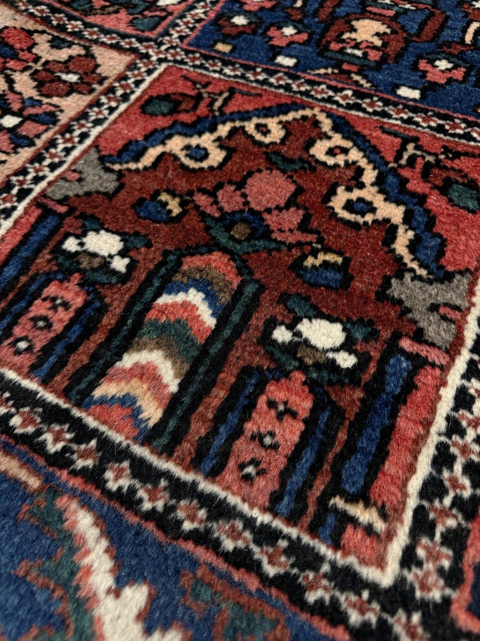 Close-up of a patterned rug with intricate designs. 10x13 handmade Persian Bakhtiari vintage rug with garden panel design, floral motifs, and red and navy tones — shown in living room at Indigo Rugs, Burlingame — San Francisco Bay Area with free shipping