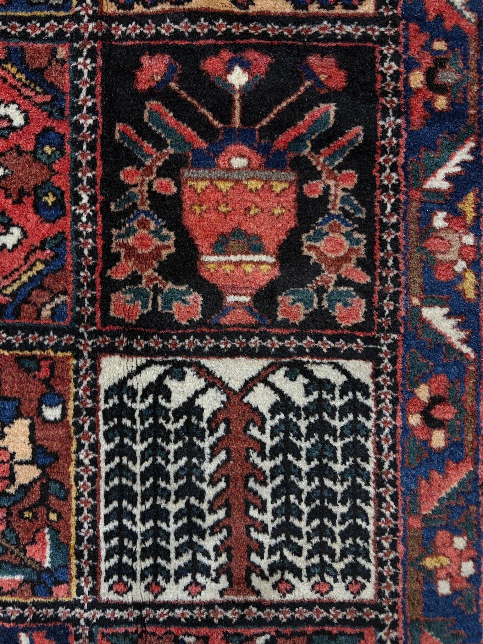 Close-up of a patterned rug with intricate designs. 10x13 handmade Persian Bakhtiari vintage rug with garden panel design, floral motifs, and red and navy tones — shown in living room at Indigo Rugs, Burlingame — San Francisco Bay Area with free shipping