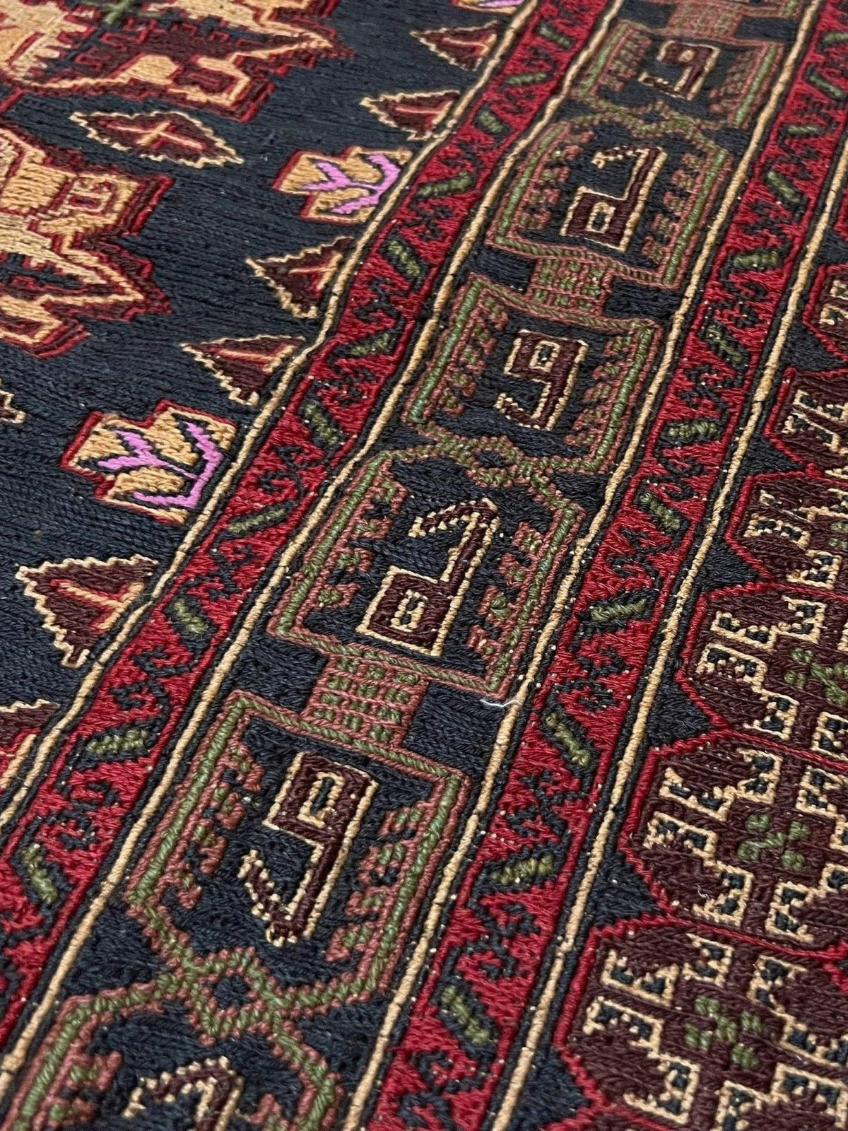 Close-up of a patterned area rug with geometric and tribal-style motifs in dark navy, red, beige, green, and purple.