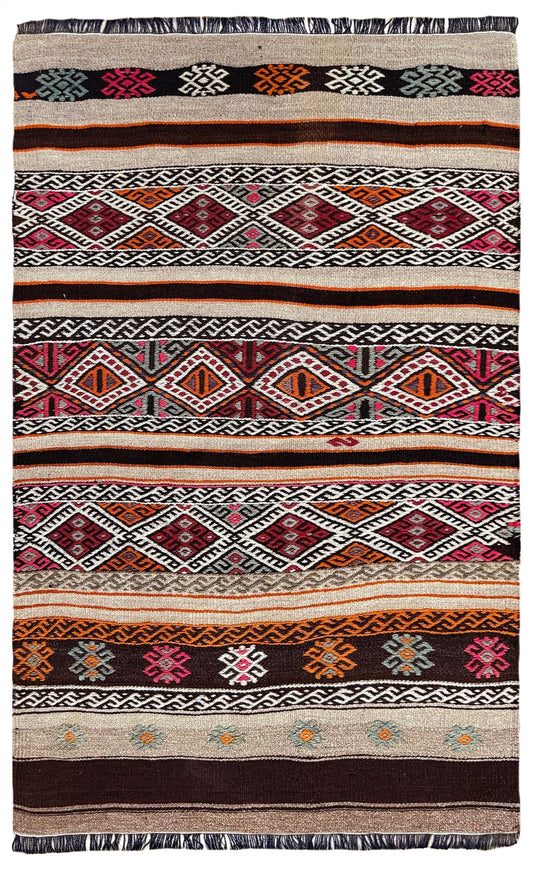 A flatweave kilim rug with a complex geometric pattern featuring multiple horizontal bands of diamonds, zigzags, and floral motifs in red, orange, pink, black, white, and beige.