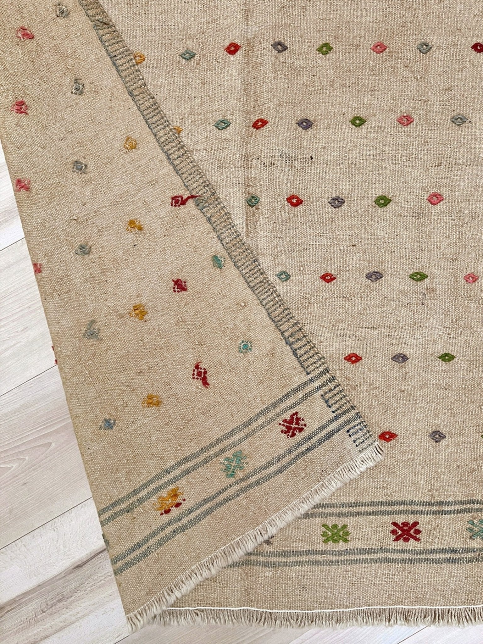 Beige rug with colorful geometric patterns on a wooden floor. Vintage Turkish neutral kilim rug, 4x6, with small colorful tribal motifs on a natural wool background.