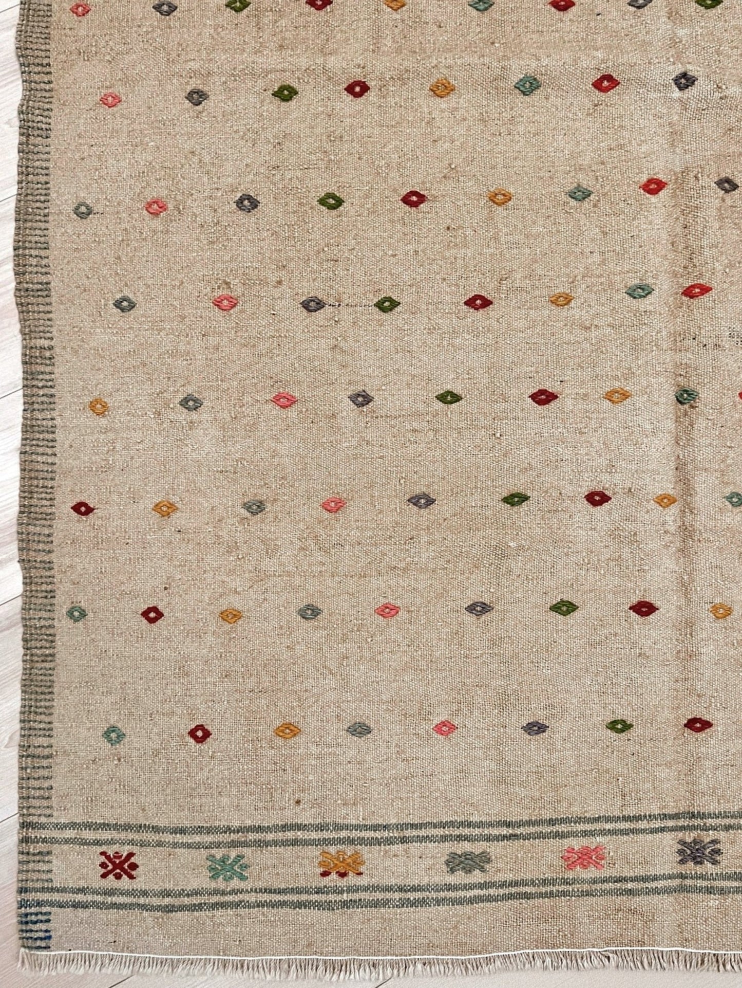 Textured fabric with geometric pattern and fringes on a plain background. Vintage Turkish neutral kilim rug, 4x6, with small colorful tribal motifs on a natural wool background.