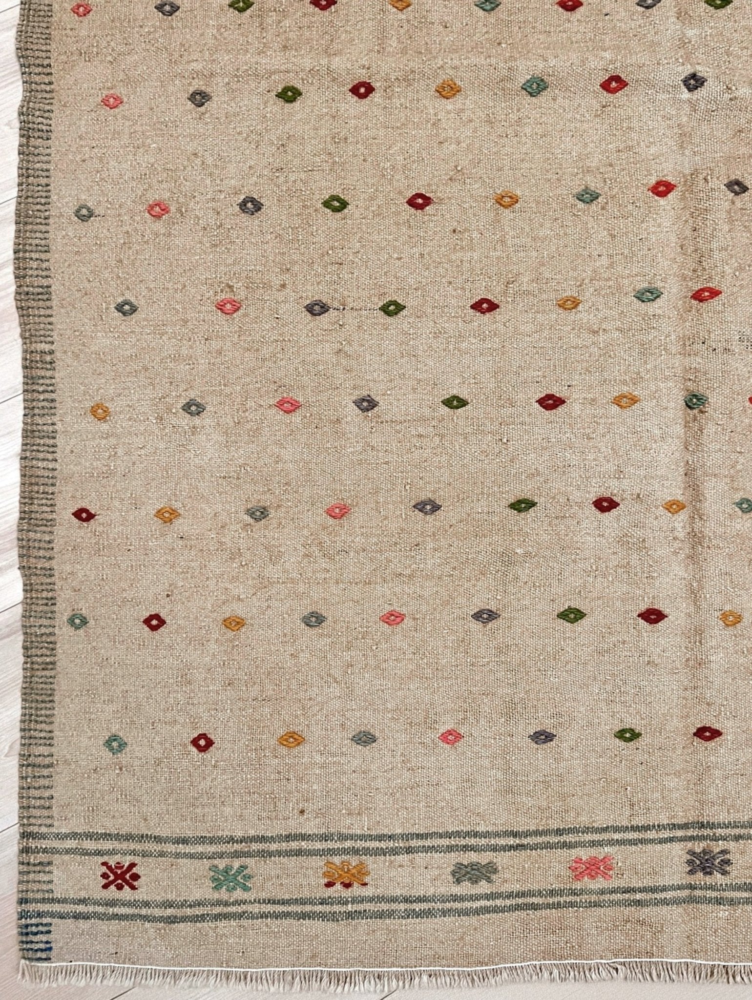 Textured fabric with geometric pattern and fringes on a plain background. Vintage Turkish neutral kilim rug, 4x6, with small colorful tribal motifs on a natural wool background.