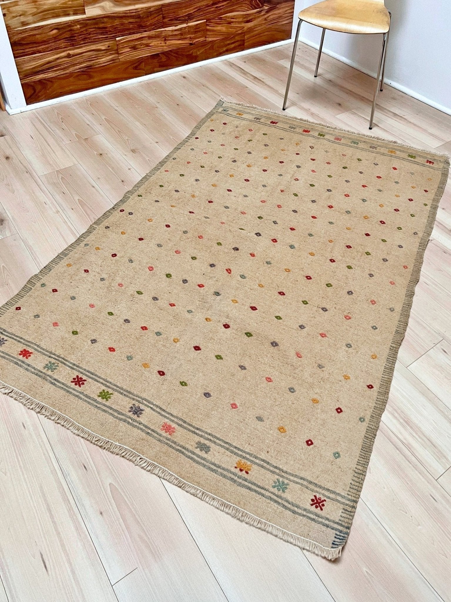 Beige area rug with colorful patterns on a wooden floor. Vintage Turkish neutral kilim rug, 4x6, with small colorful tribal motifs on a natural wool background.