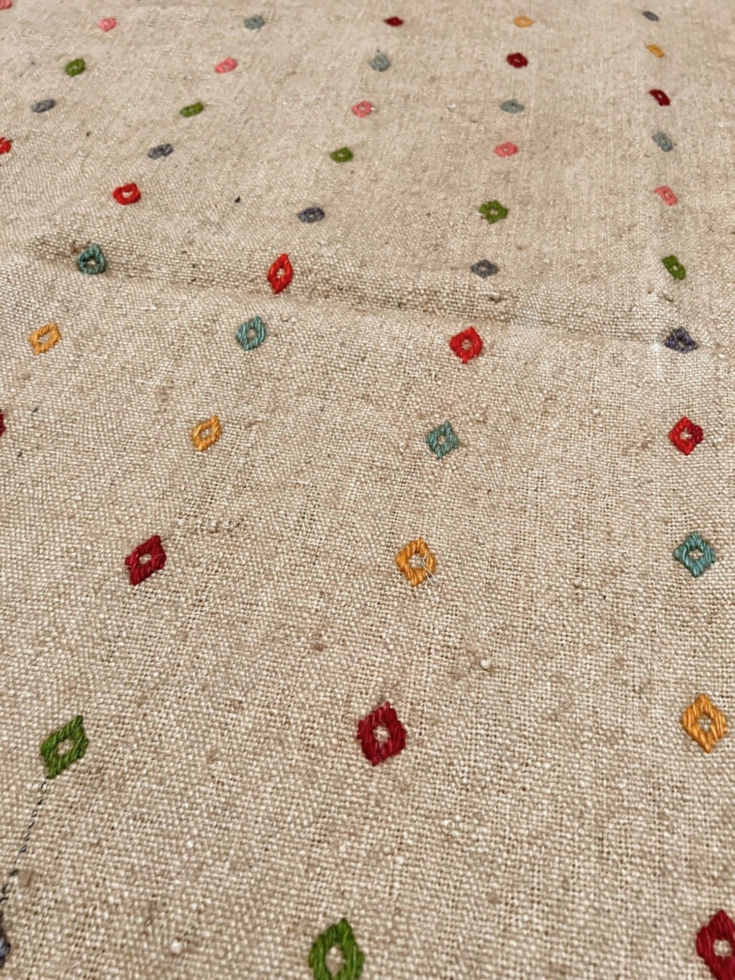 Textured fabric with small colorful embroidered patterns. Vintage Turkish neutral kilim rug, 4x6, with small colorful tribal motifs on a natural wool background.