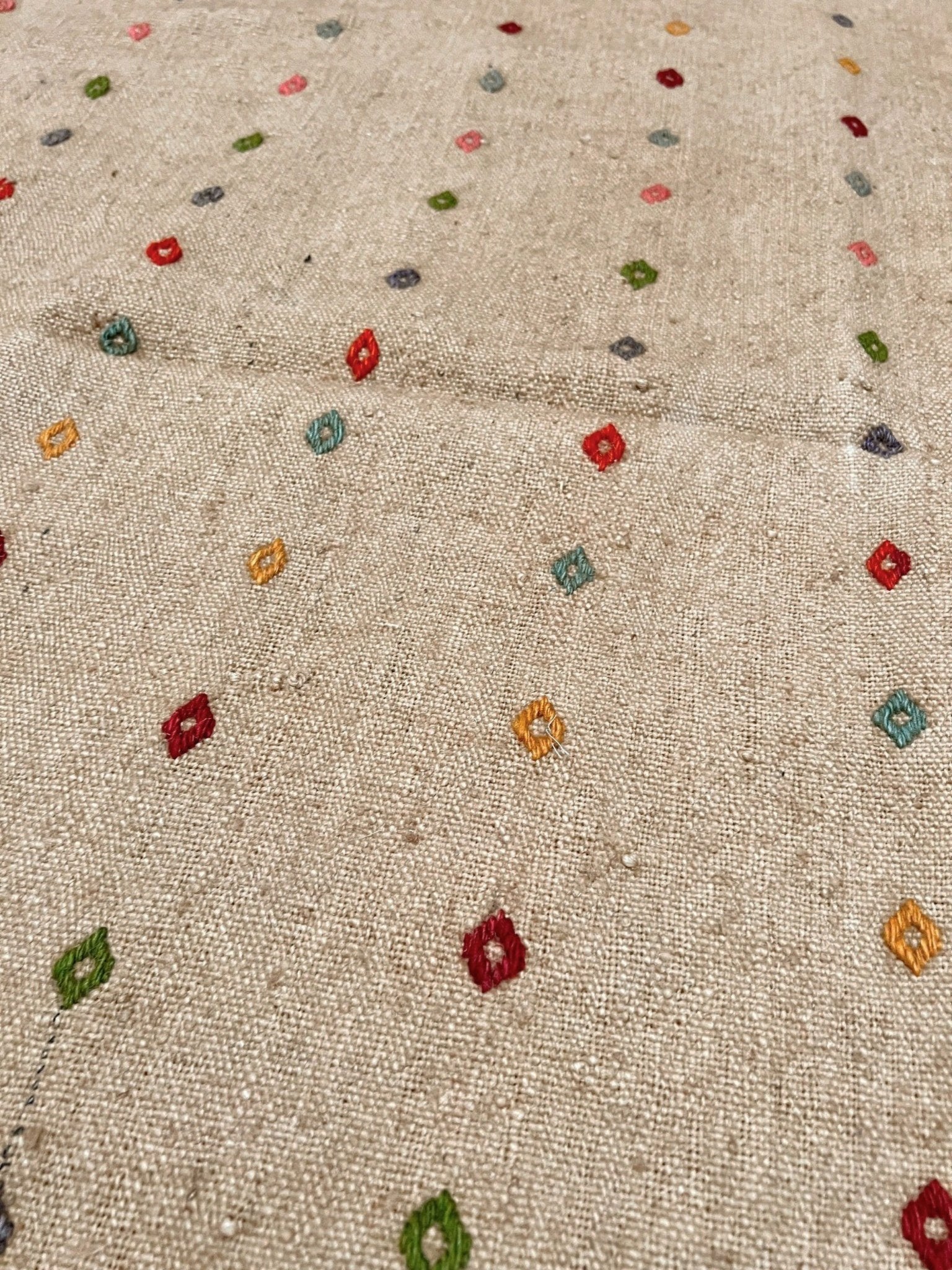 Textured fabric with small colorful embroidered patterns. Vintage Turkish neutral kilim rug, 4x6, with small colorful tribal motifs on a natural wool background.