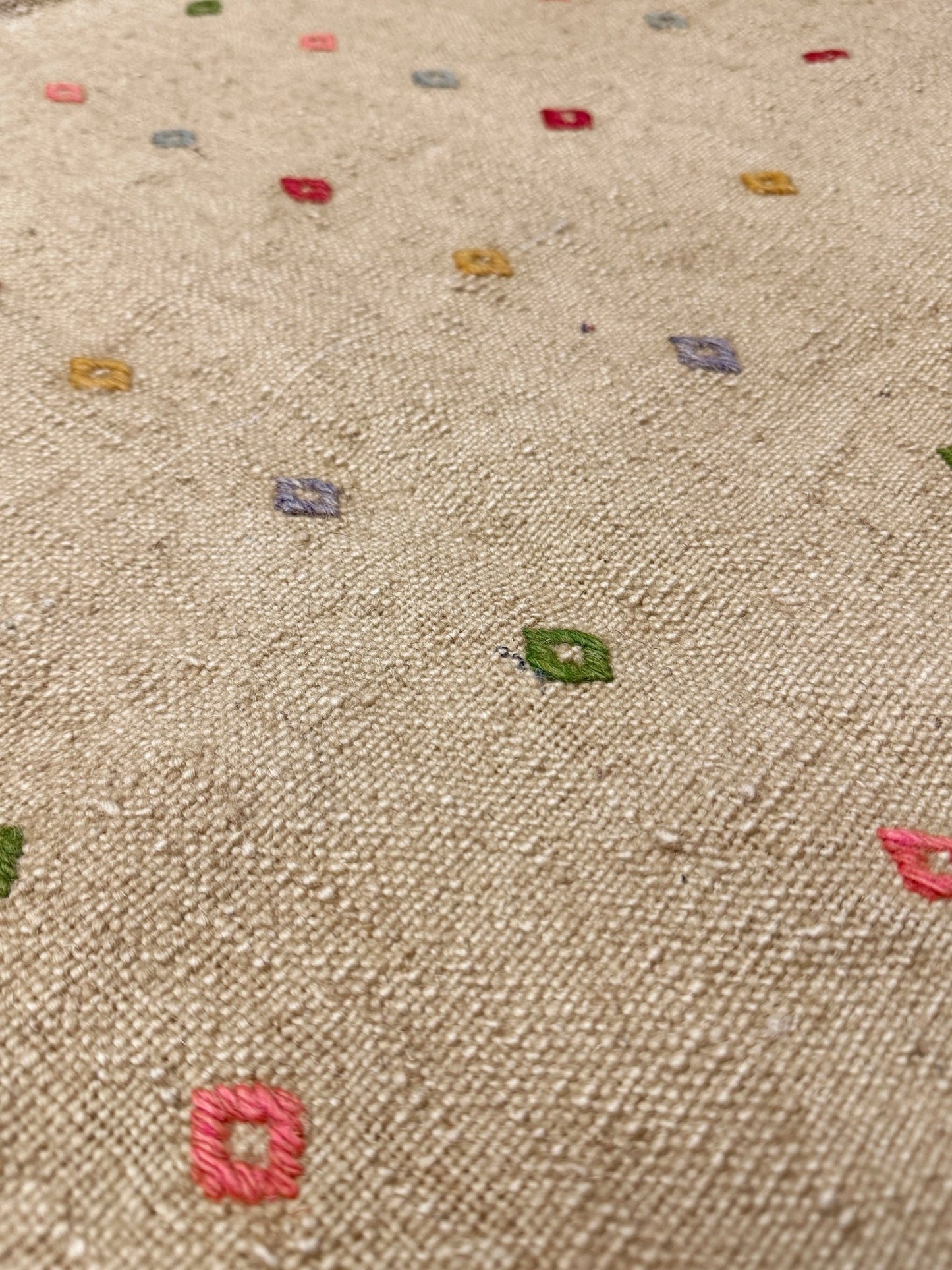 Close-up of a textured fabric with colorful embroidered patterns on a beige background. Vintage Turkish neutral kilim rug, 4x6, with small colorful tribal motifs on a natural wool background.