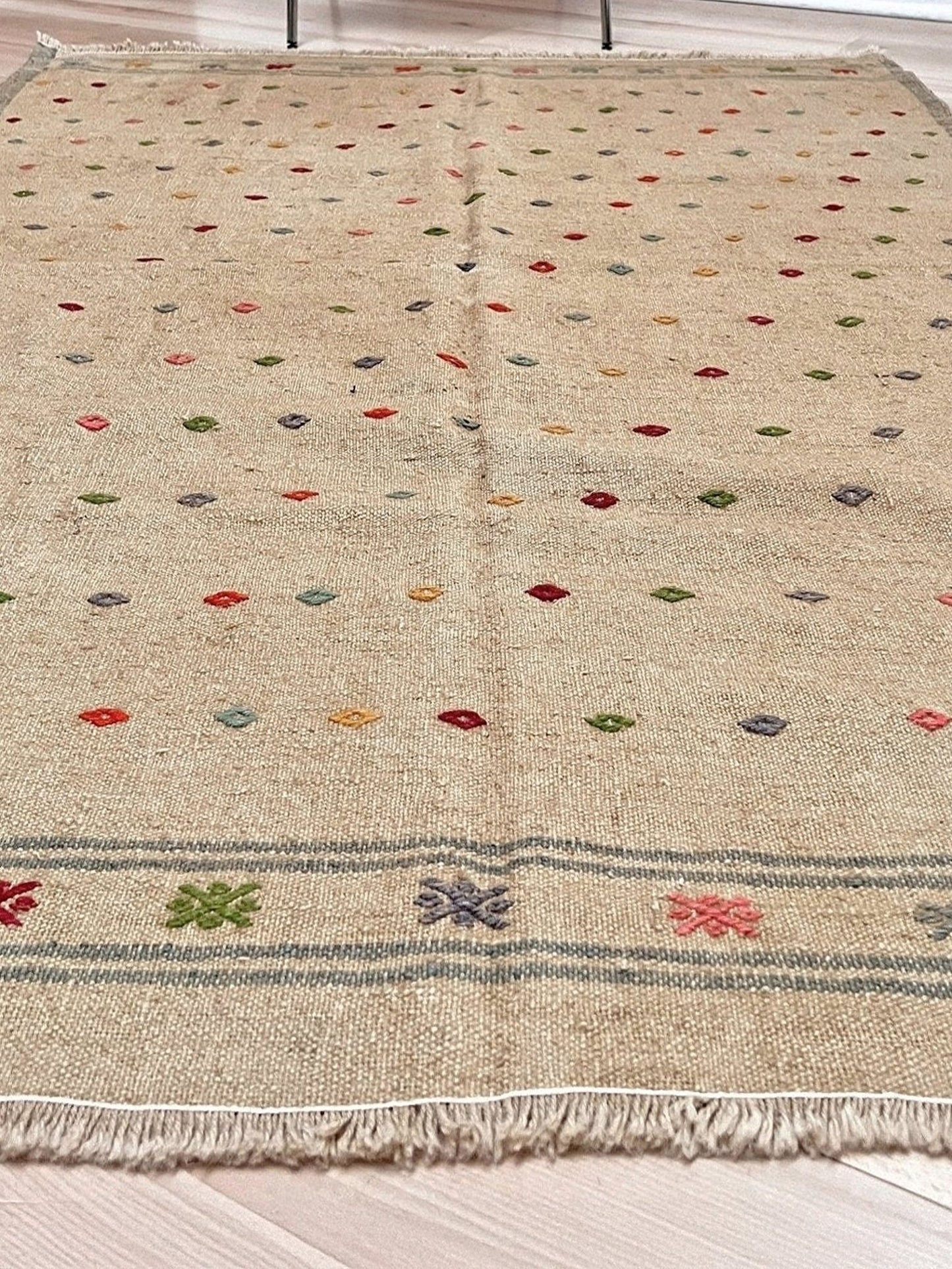 Beige rug with colorful geometric pattern on a wooden floor. Vintage Turkish neutral kilim rug, 4x6, with small colorful tribal motifs on a natural wool background.