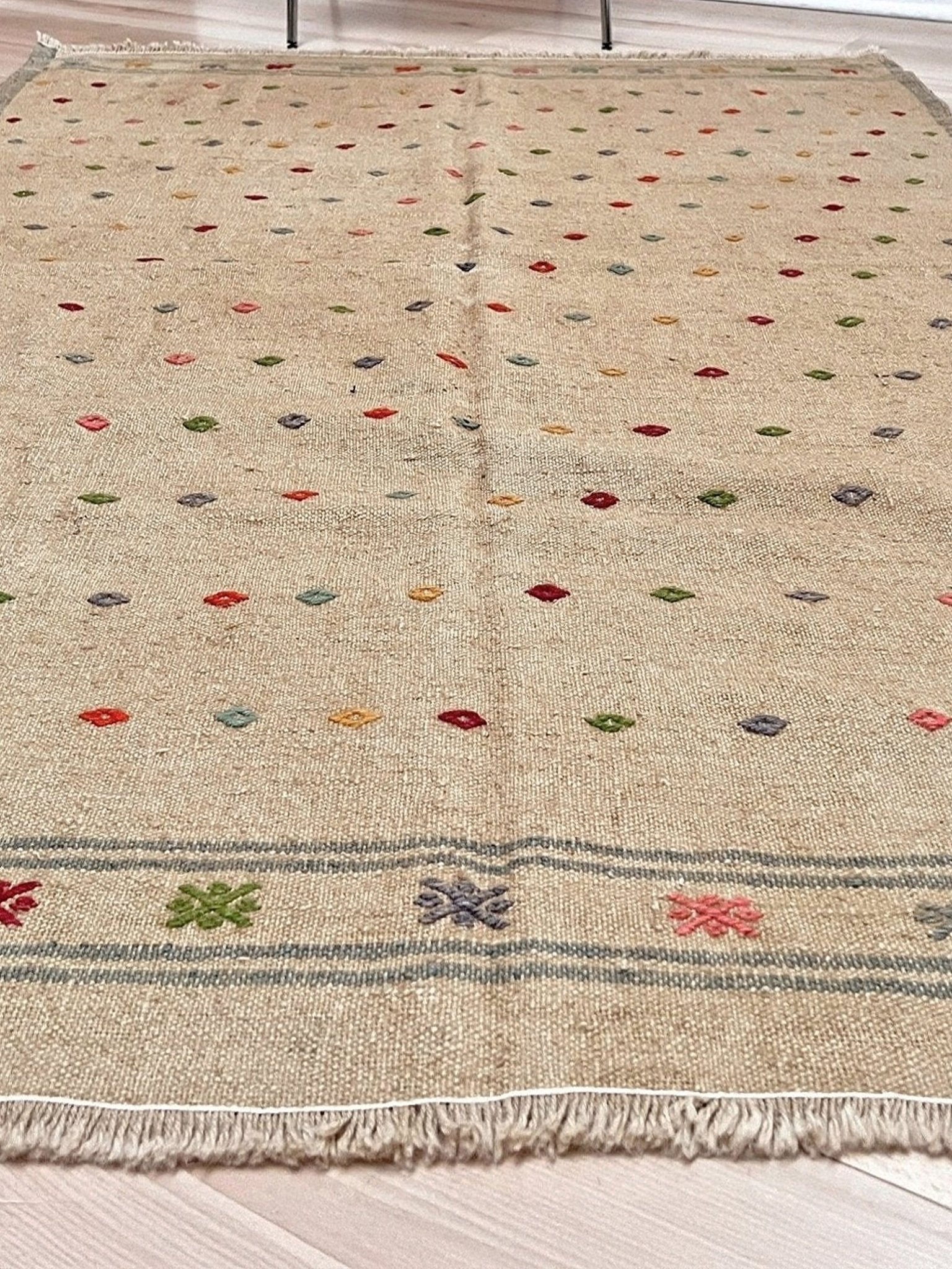 Beige rug with colorful geometric pattern on a wooden floor. Vintage Turkish neutral kilim rug, 4x6, with small colorful tribal motifs on a natural wool background.