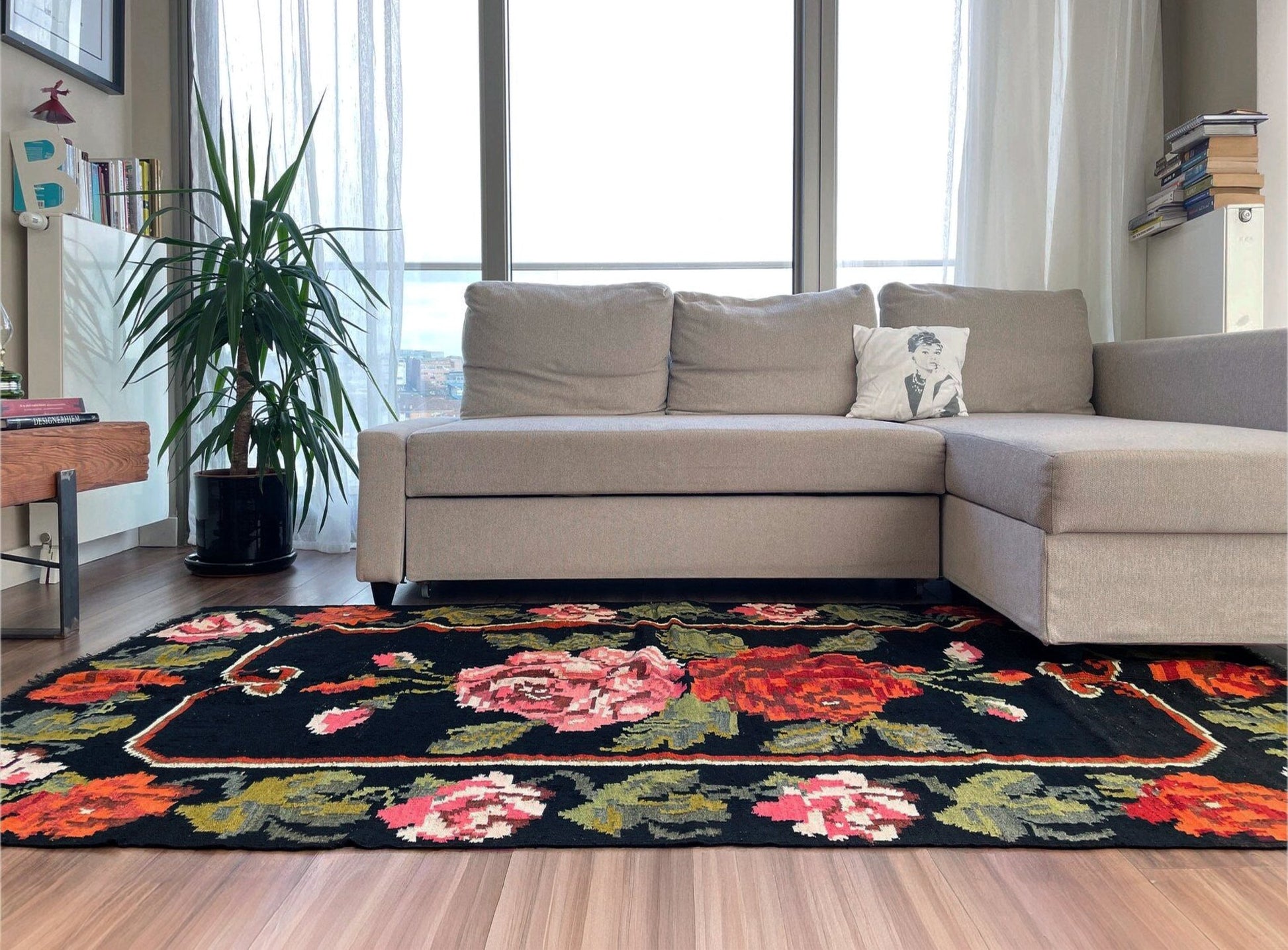 Floral rug on a wooden floor in a living room with a sectional sofa and plant. Vintage moldovan floral kilim rug 5x8 handmade rose design black background flatweave 1960s eastern european wool rug san francisco bay area rug shop indigo rugs