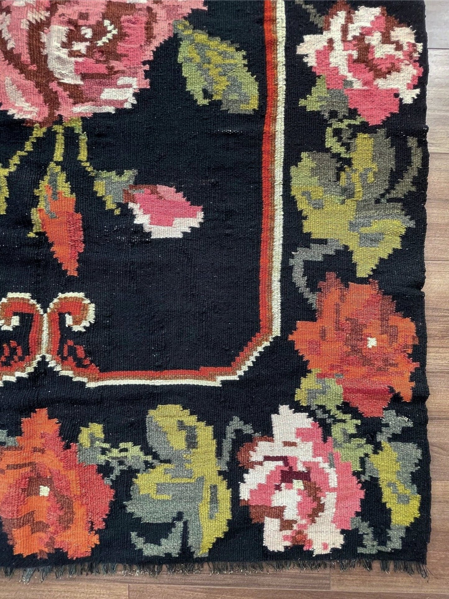 Floral patterned rug with vibrant colors on a wooden floor. Vintage moldovan floral kilim rug 5x8 handmade rose design black background flatweave 1960s eastern european wool rug san francisco bay area rug shop indigo rugs