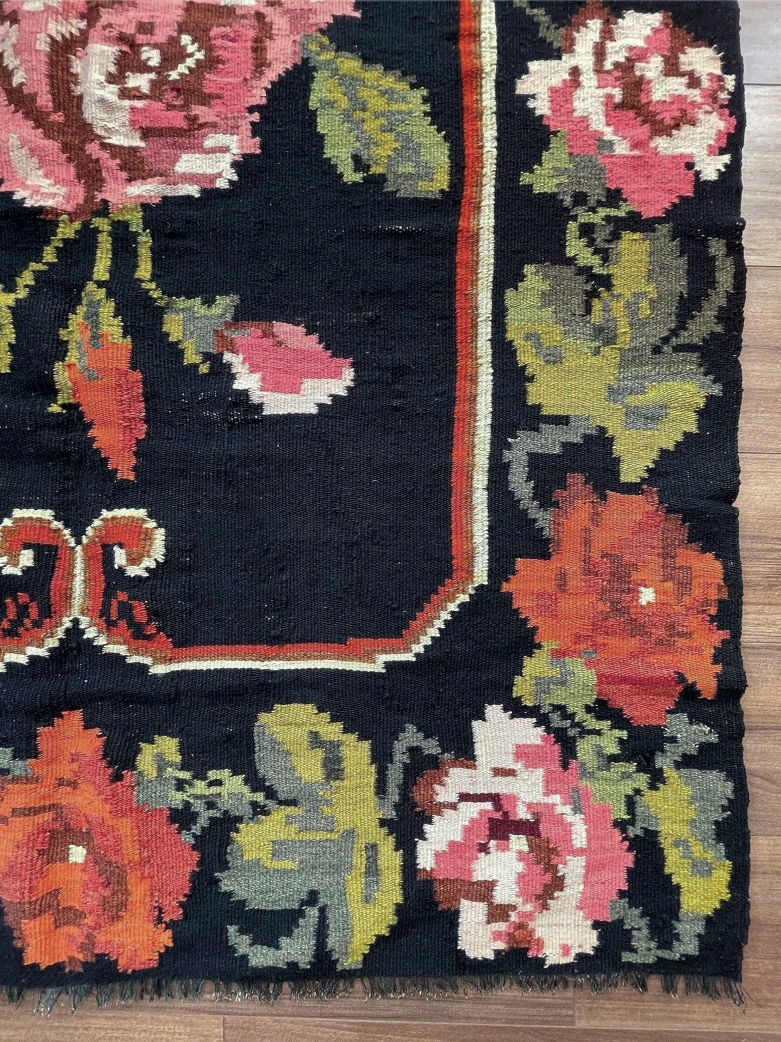 Floral patterned rug with vibrant colors on a wooden floor. Vintage moldovan floral kilim rug 5x8 handmade rose design black background flatweave 1960s eastern european wool rug san francisco bay area rug shop indigo rugs
