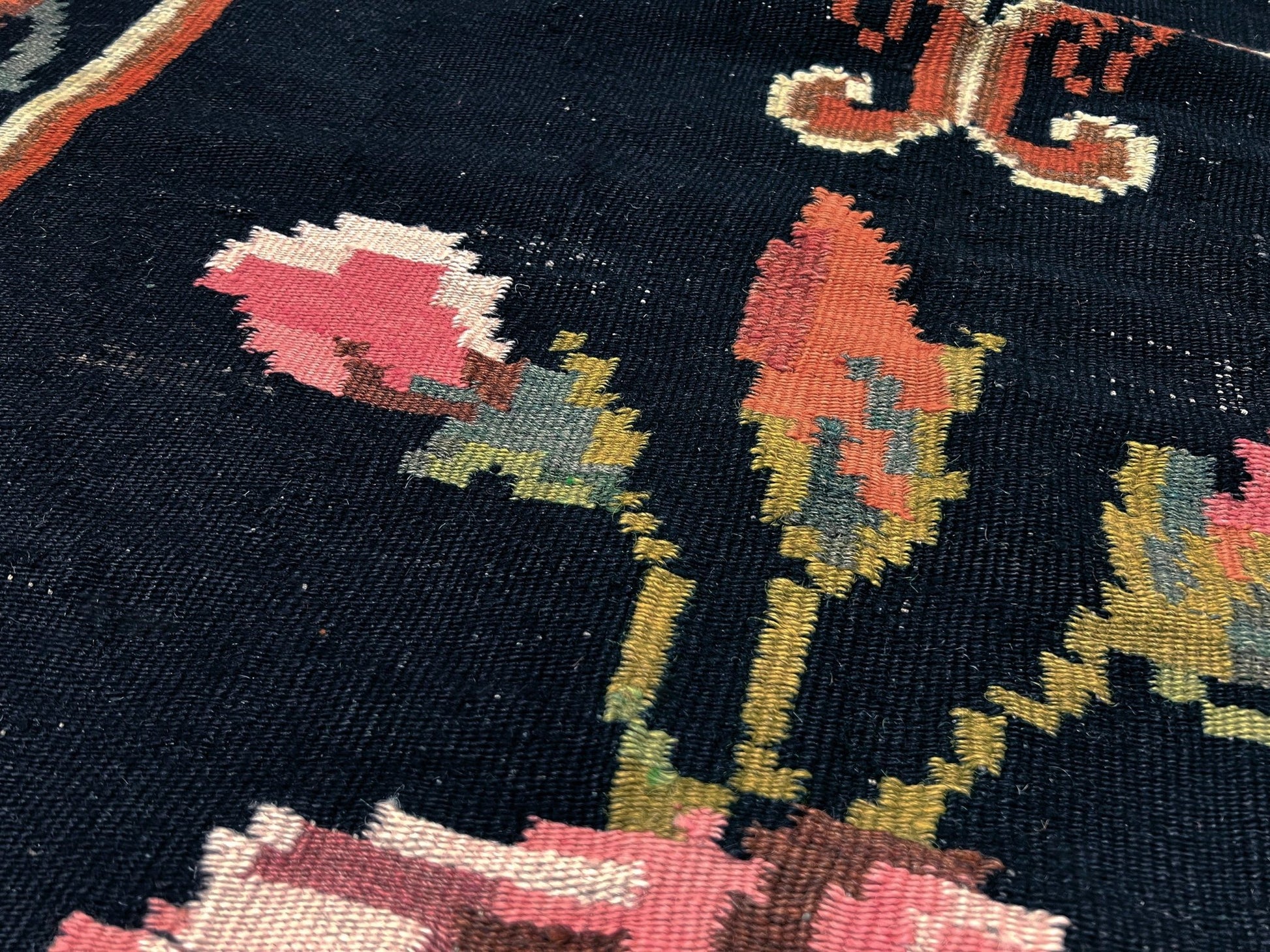 Close-up of a patterned fabric with floral designs on a dark background. Vintage moldovan floral kilim rug 5x8 handmade rose design black background flatweave 1960s eastern european wool rug san francisco bay area rug shop indigo rugs
