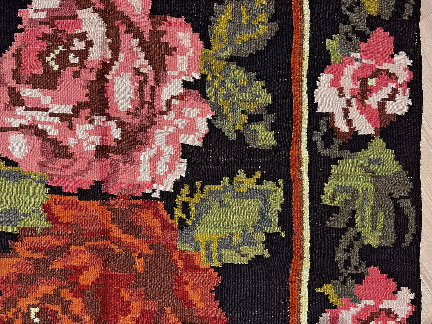 Close-up of a floral patterned fabric with pink, green, and brown colors on a black background. Vintage moldovan floral kilim rug 5x8 handmade rose design black background flatweave 1960s eastern european wool rug san francisco bay area rug shop indigo rugs