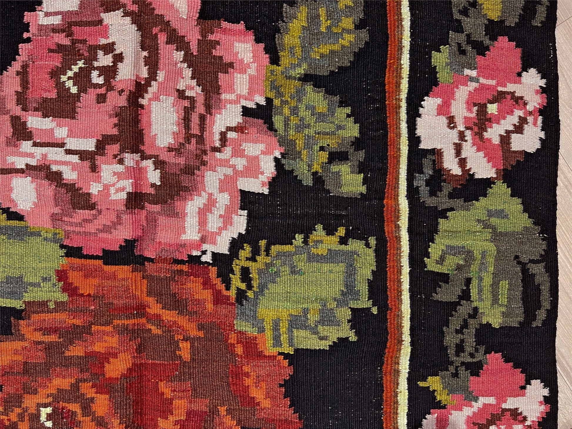 Close-up of a floral patterned fabric with pink, green, and brown colors on a black background. Vintage moldovan floral kilim rug 5x8 handmade rose design black background flatweave 1960s eastern european wool rug san francisco bay area rug shop indigo rugs