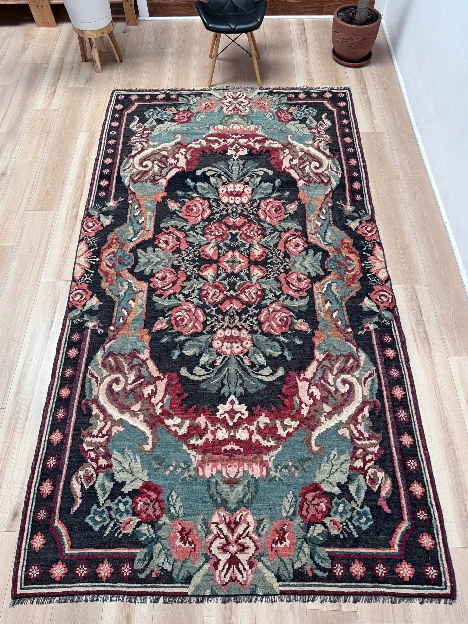 A rectangular traditional area rug with an ornate floral medallion pattern, laid out on a light wood floor in a room setting. Vintage Moldovan rose kilim floral rug handmade wool flatweave 6x10  from Indigo Rugs Burlingame Bay Area.