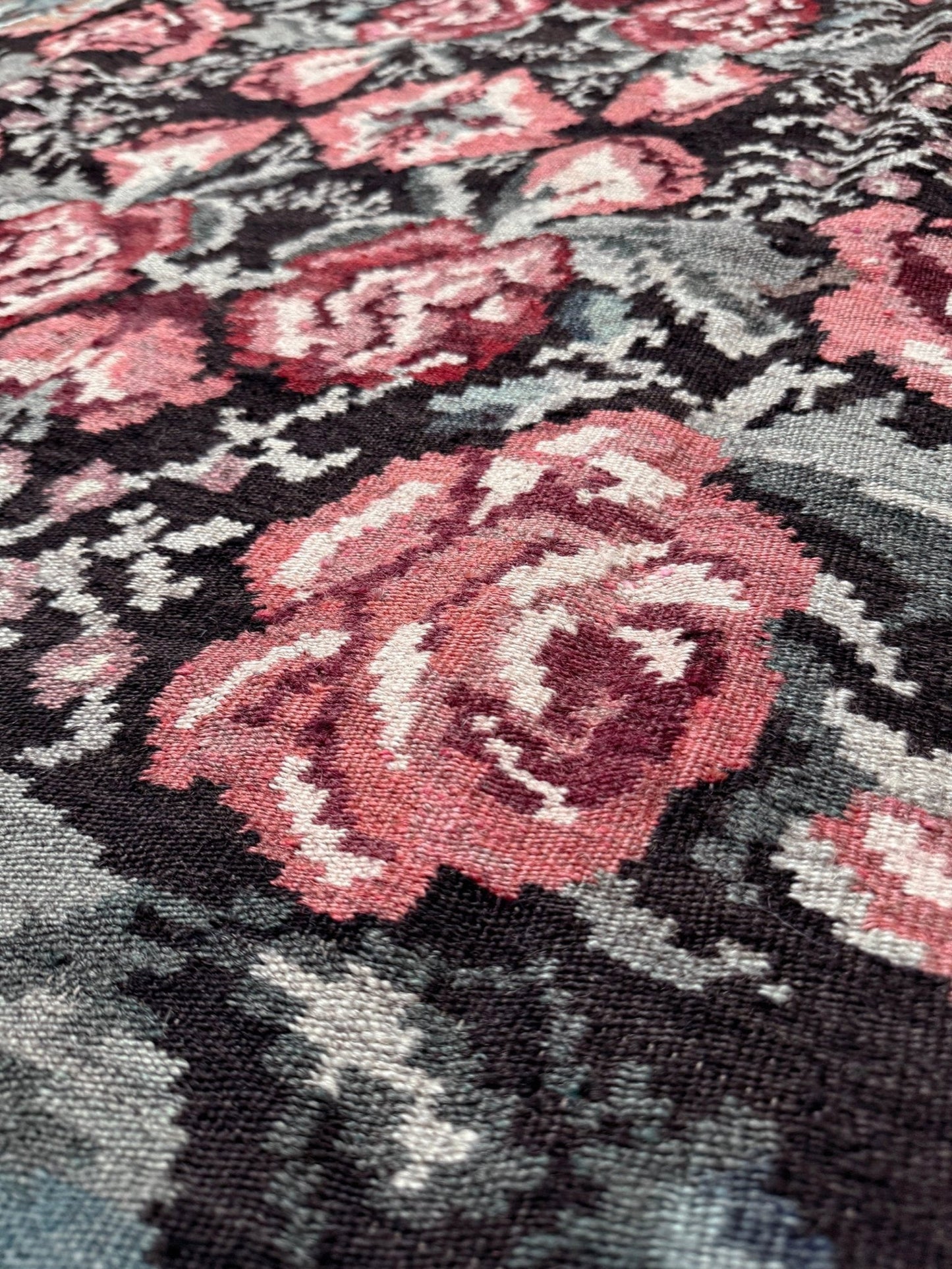 Close-up of a woven floral textile pattern with large pink and burgundy roses on a dark charcoal background with gray and off-white details. Vintage Moldovan rose kilim floral rug handmade wool flatweave 6x10  from Indigo Rugs Burlingame Bay Area.