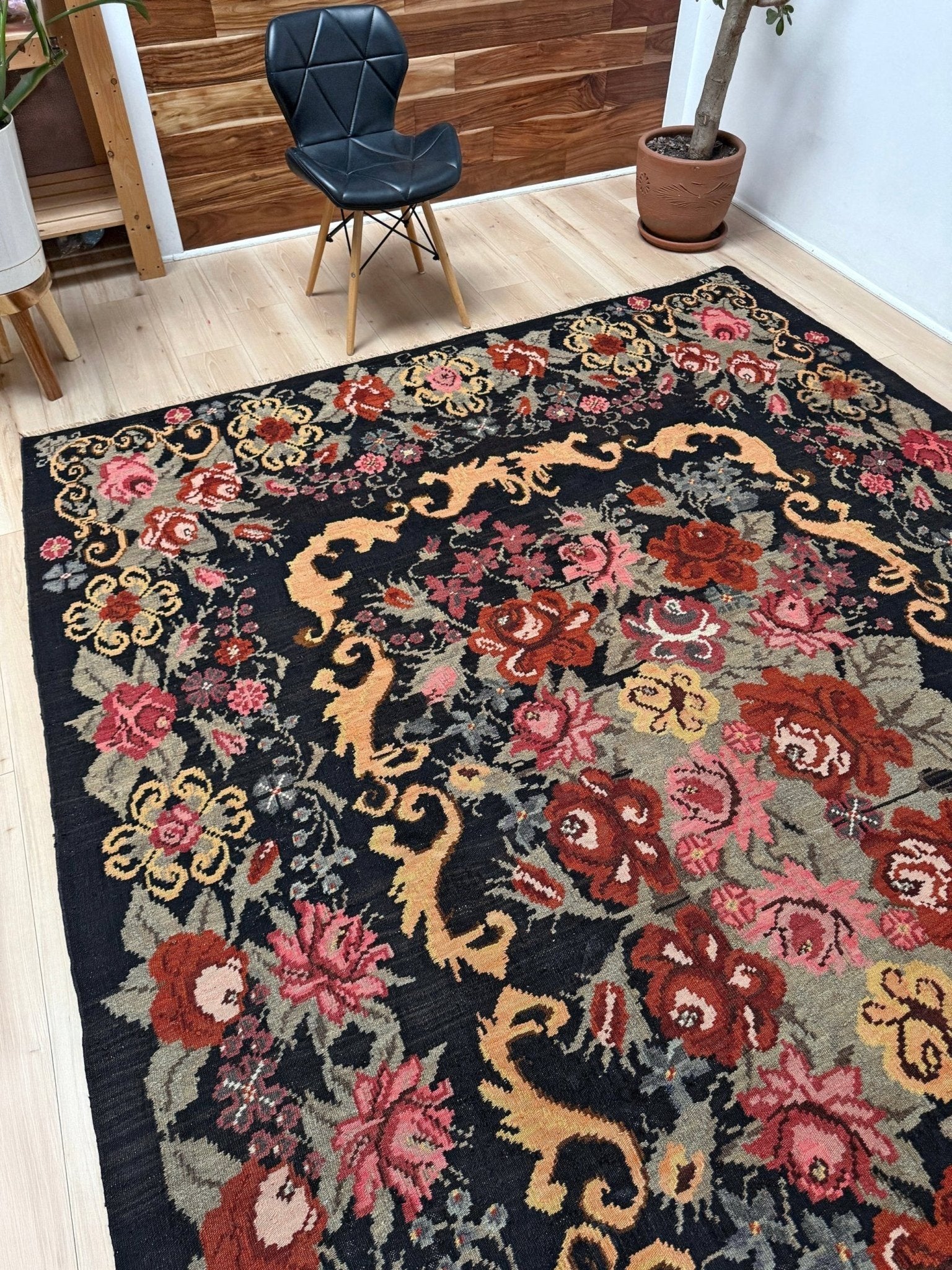 Decorative floral moldovan rose kilim rug on a wooden floor with a chair and plant in the background