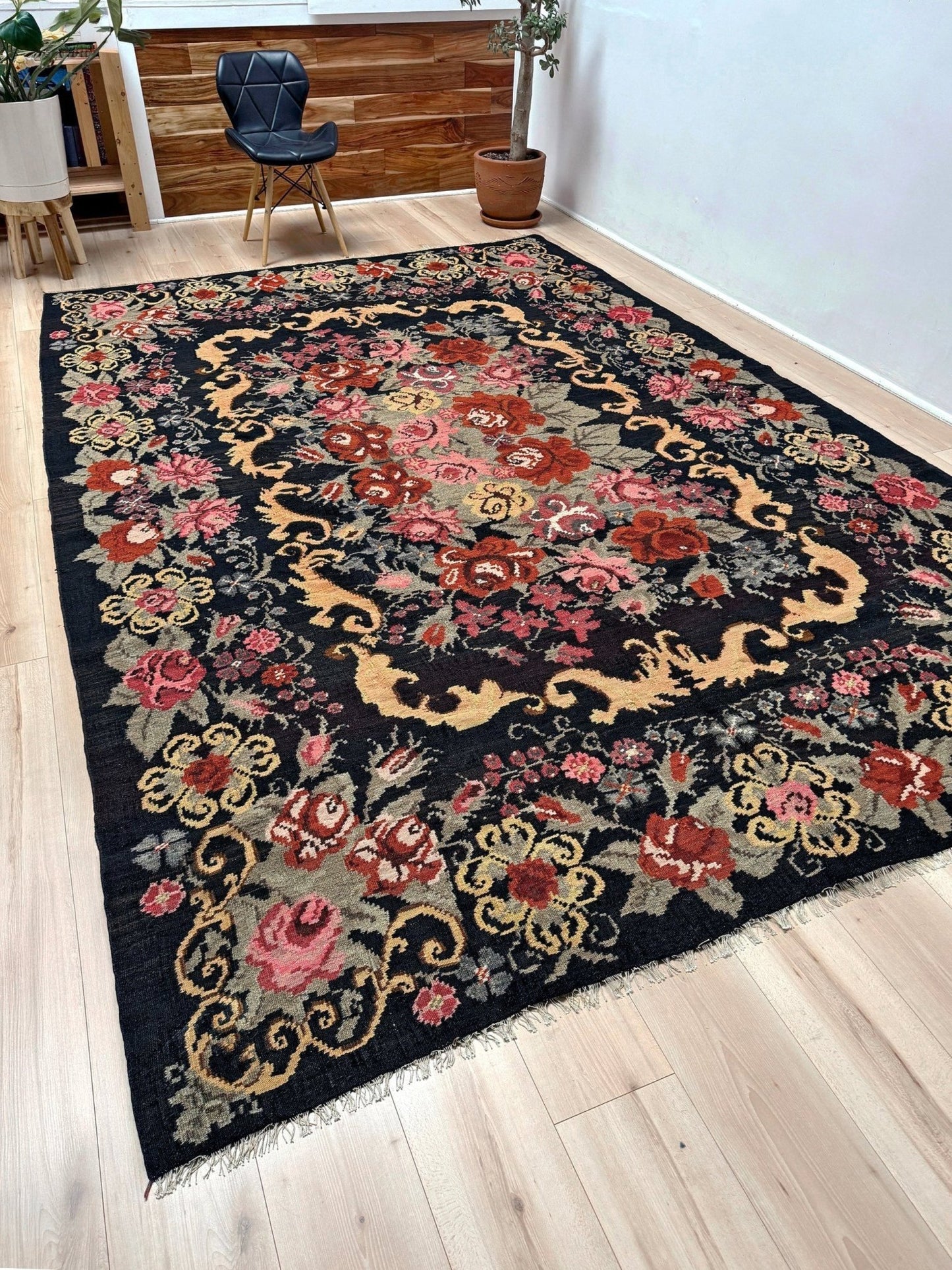 Decorative floral moldovan rose kilim rug on a wooden floor with a chair and plant in the background.