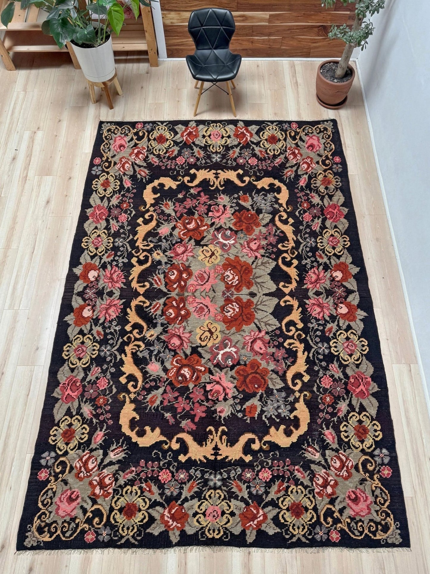 Decorative floral moldovan rose kilim rug on a wooden floor with a chair and plants in the background