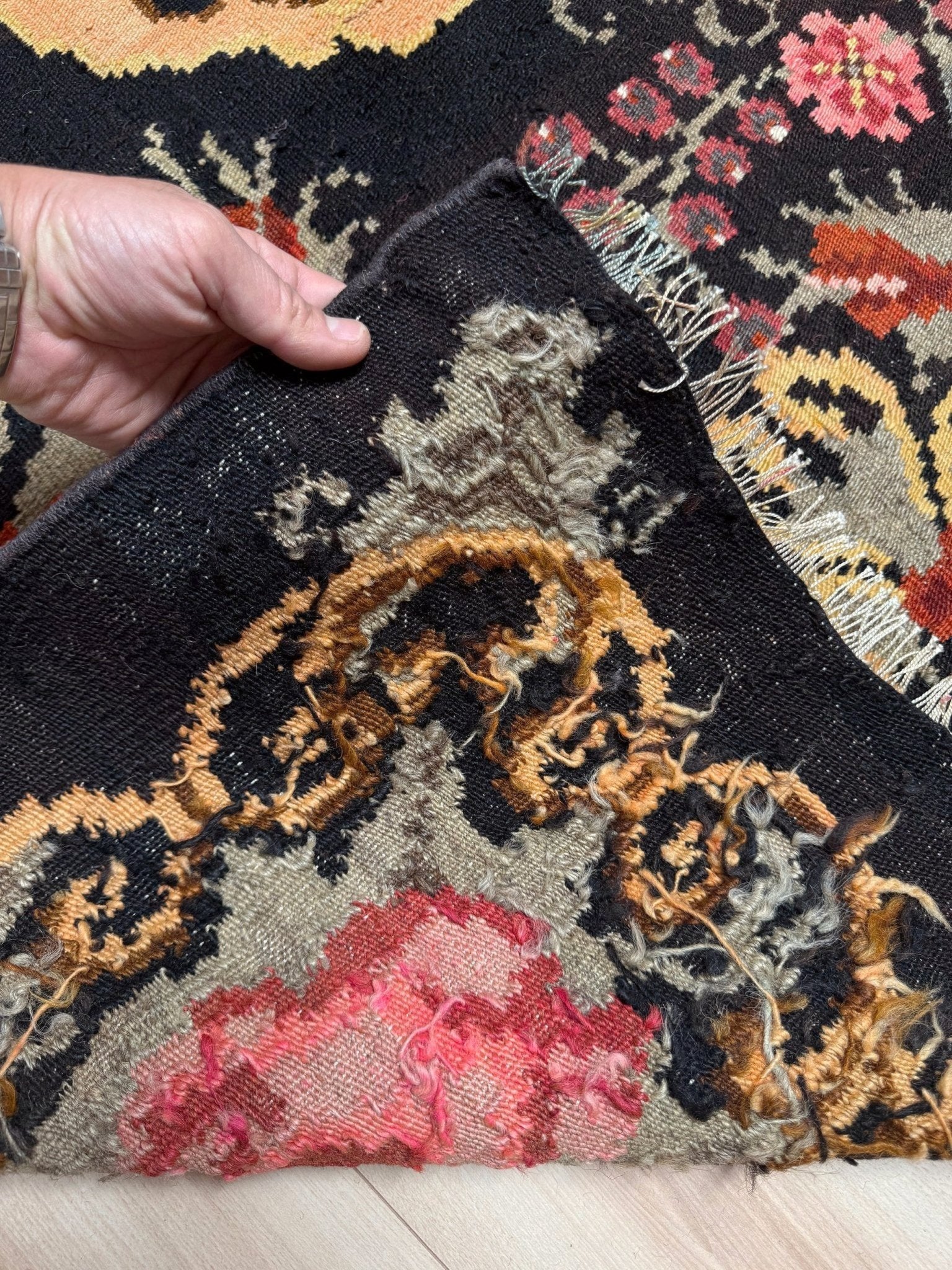 Hand holding a corner of an ornate moldovan rose kilim rug with floral patterns.