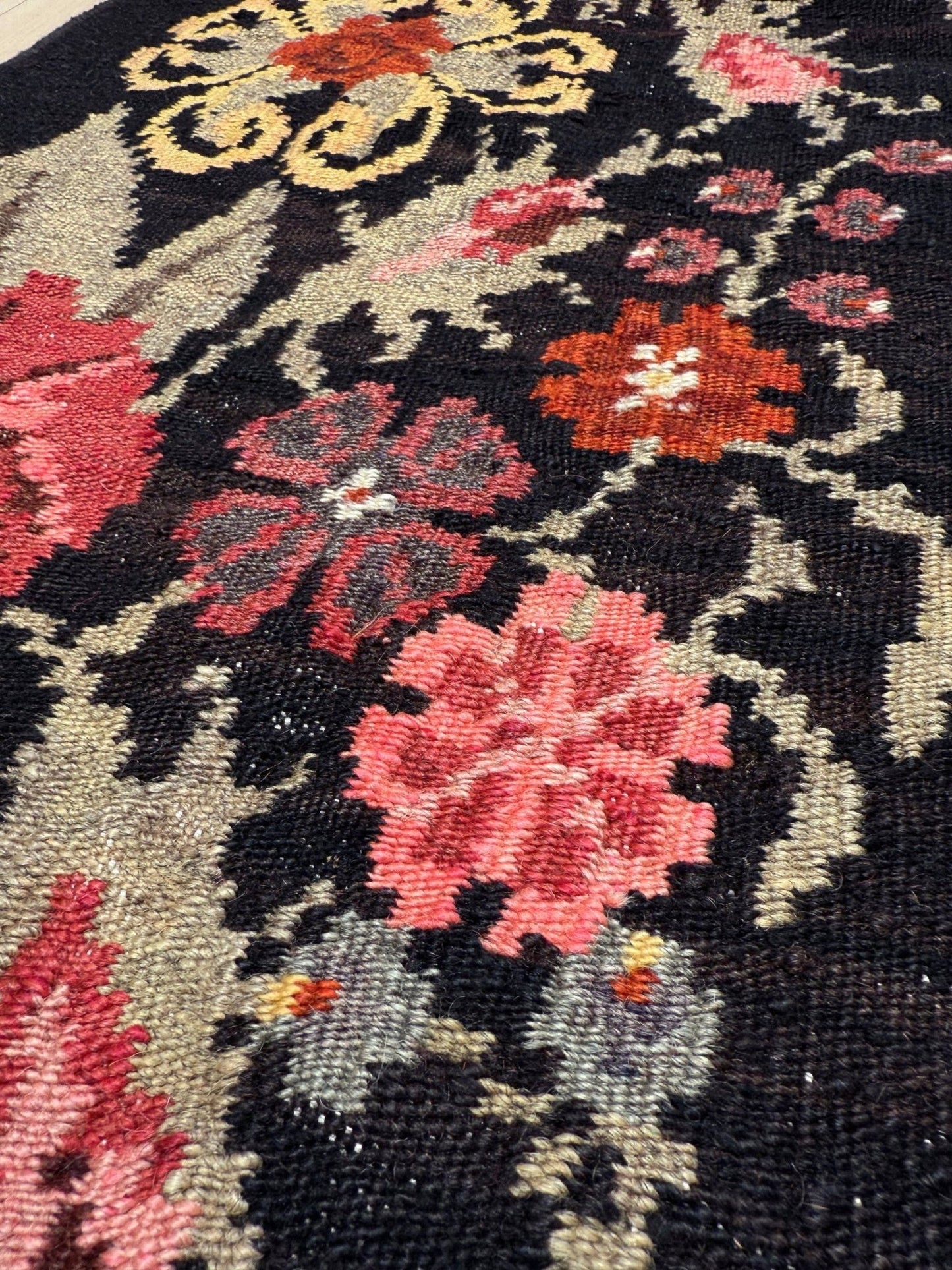 Close-up of a floral patterned moldovan rose kilim rug with red, pink, and yellow flowers on a black background.