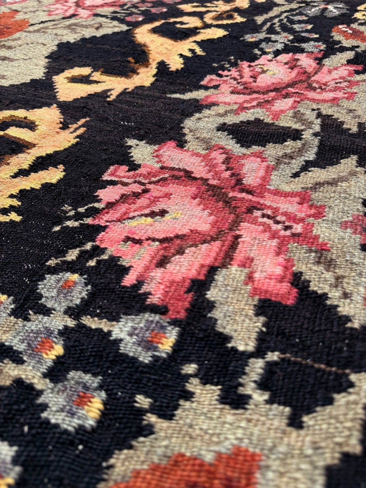 Close-up of a floral patterned moldovan rose kilim rug with pink flowers on a black background