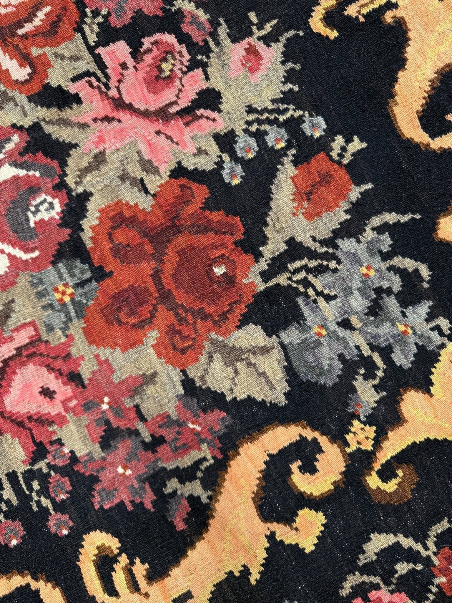 Close-up of a floral patterned moldovan rose kilim rug with red, pink, and gold colors on a black background.