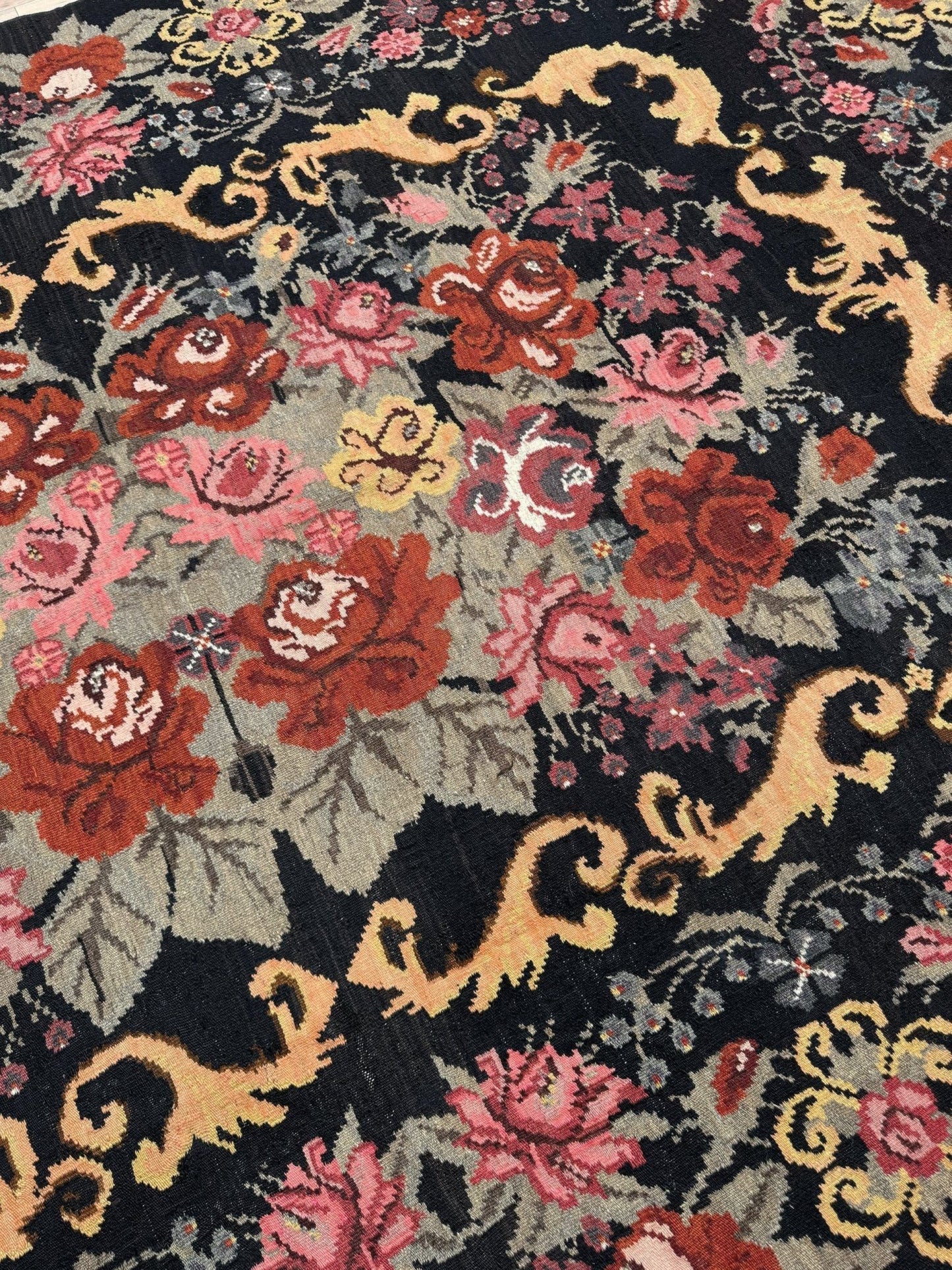 Close-up of a floral patterned moldovan rose kilim rug with red, pink, and gold colors on a black background.