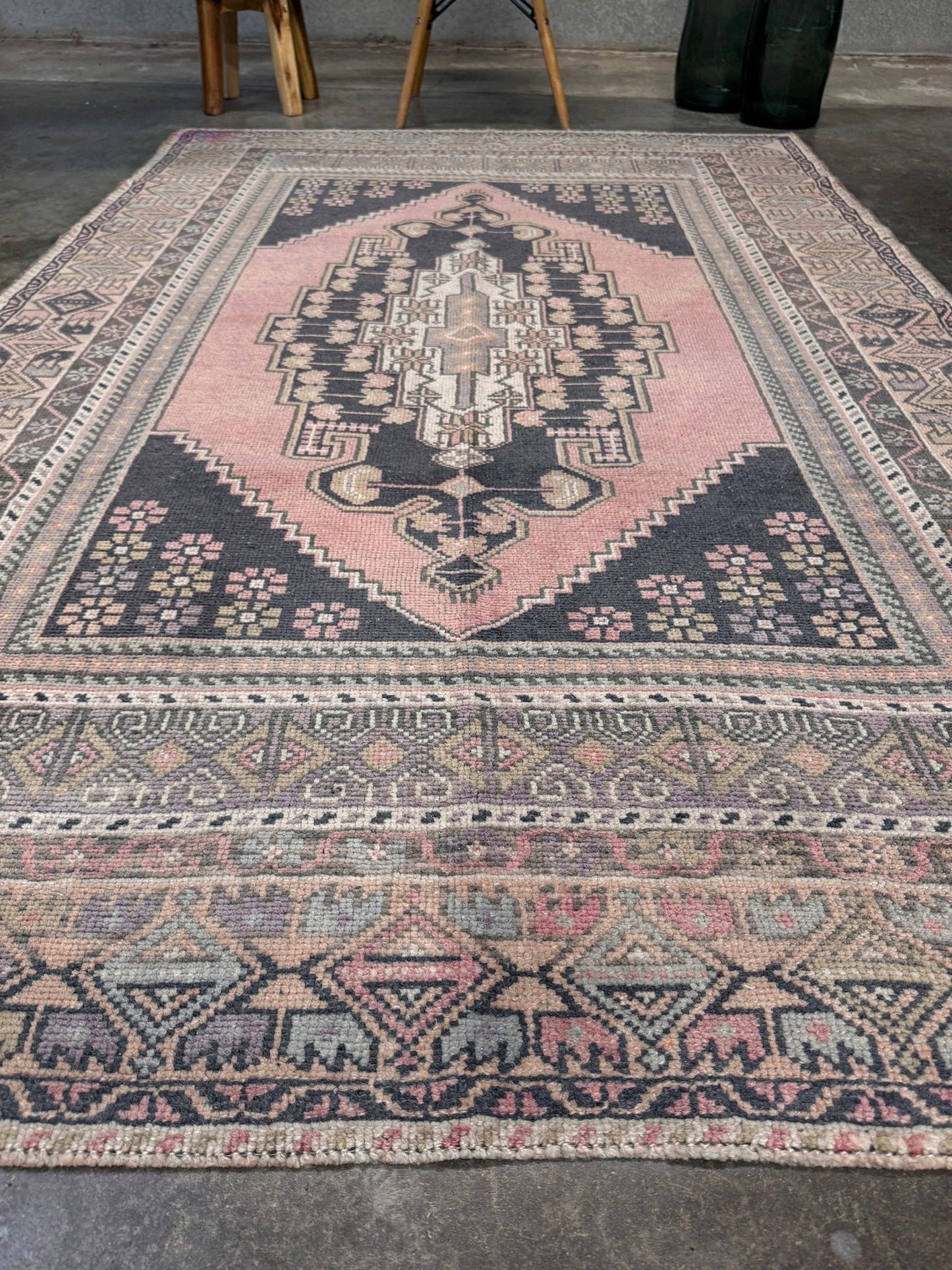 Patterned rug with geometric design on a gray floor. pastel vintage turkish obruk rug 4x7 handwoven anatolian wool rug dusty rose field charcoal navy medallion floral border low pile vintage rug indigo rugs san francisco bay area