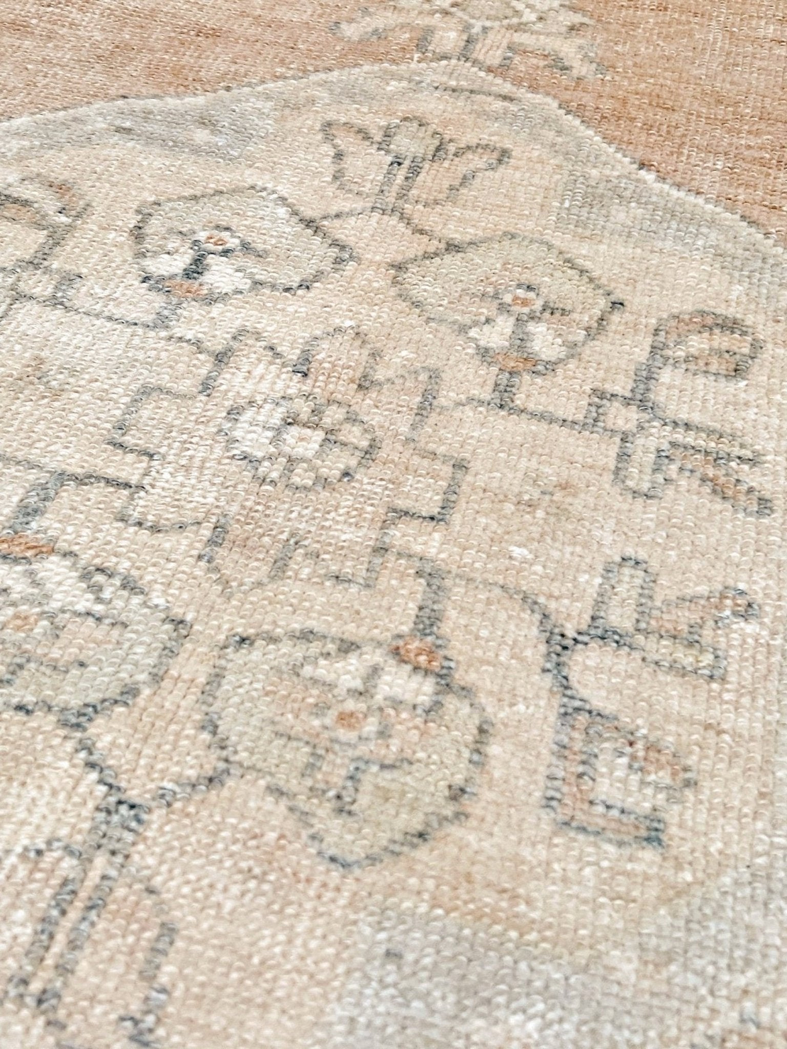 Close-up of a vintage-style area rug with a distressed floral pattern in beige, cream, and muted gray tones.