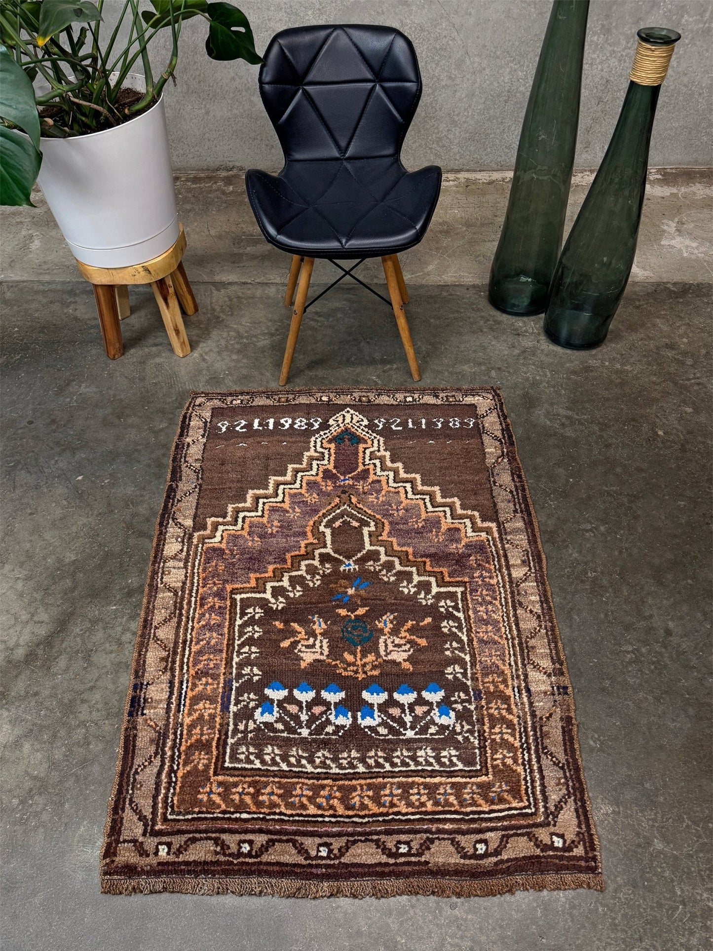 Decorative rug with intricate patterns on a concrete floor, surrounded by a black chair, plant, and vase. 3x4 Kars Wool vintage turkish mini rug. Handmade turkish rug shop san francisco bay area. Buy handmade wool rug online