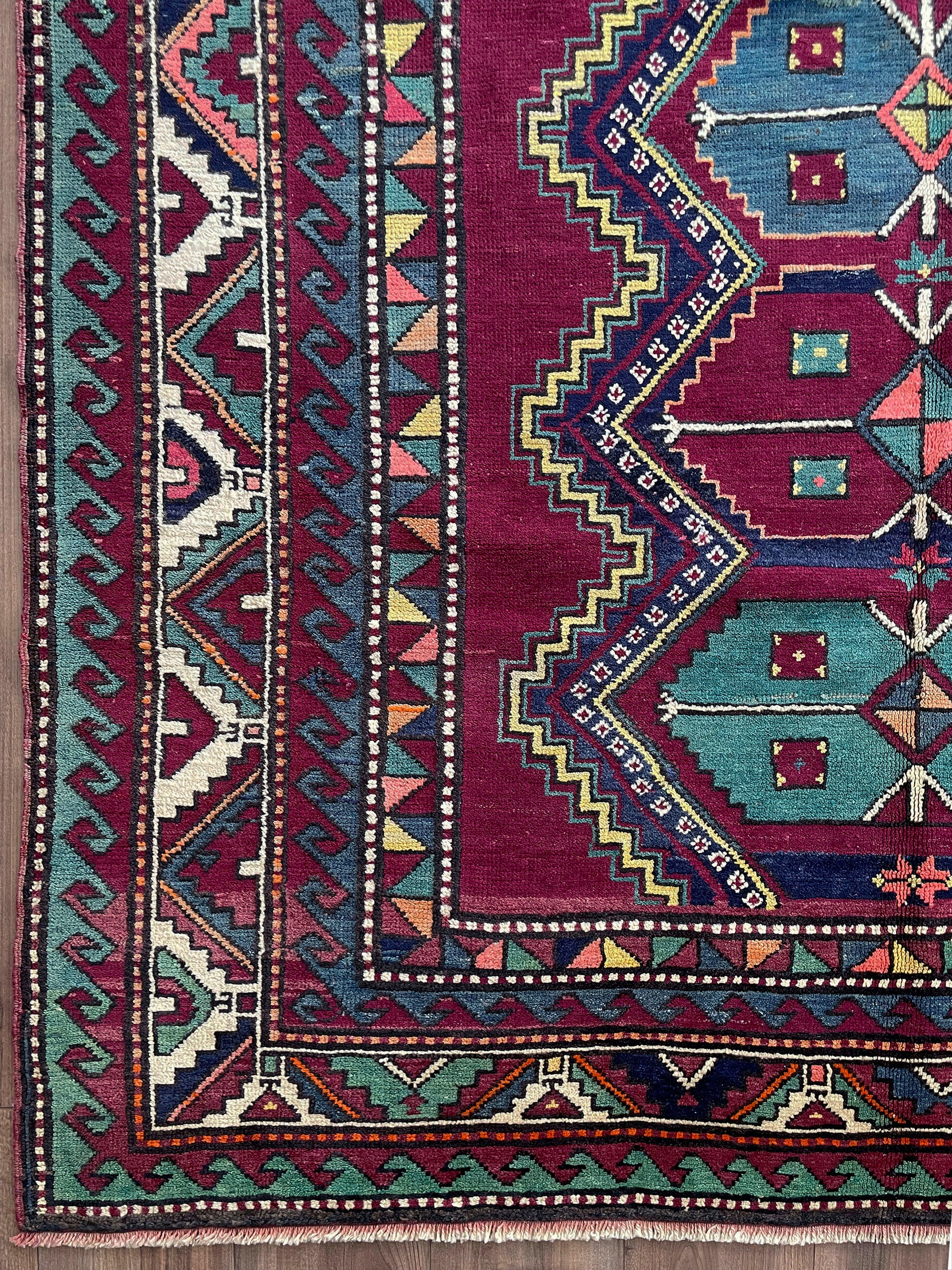 Colorful patterned rug with geometric designs on a wooden floor. vintage kazak caucasian rug 6x9 burgundy field tribal geometric handmade wool 1940s antique style rug san francisco bay area rug shop indigo rugs