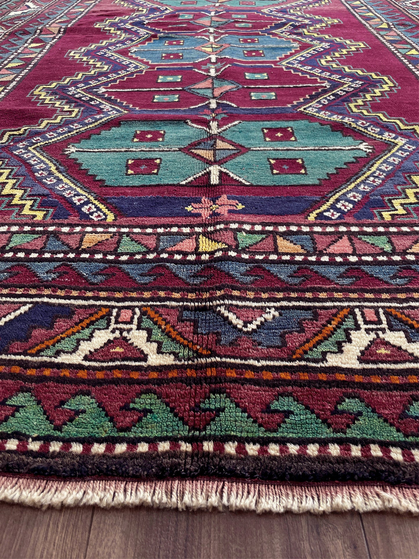 Close-up of a colorful patterned rug with geometric designs on a wooden floor. vintage kazak caucasian rug 6x9 burgundy field tribal geometric handmade wool 1940s antique style rug san francisco bay area rug shop indigo rugs