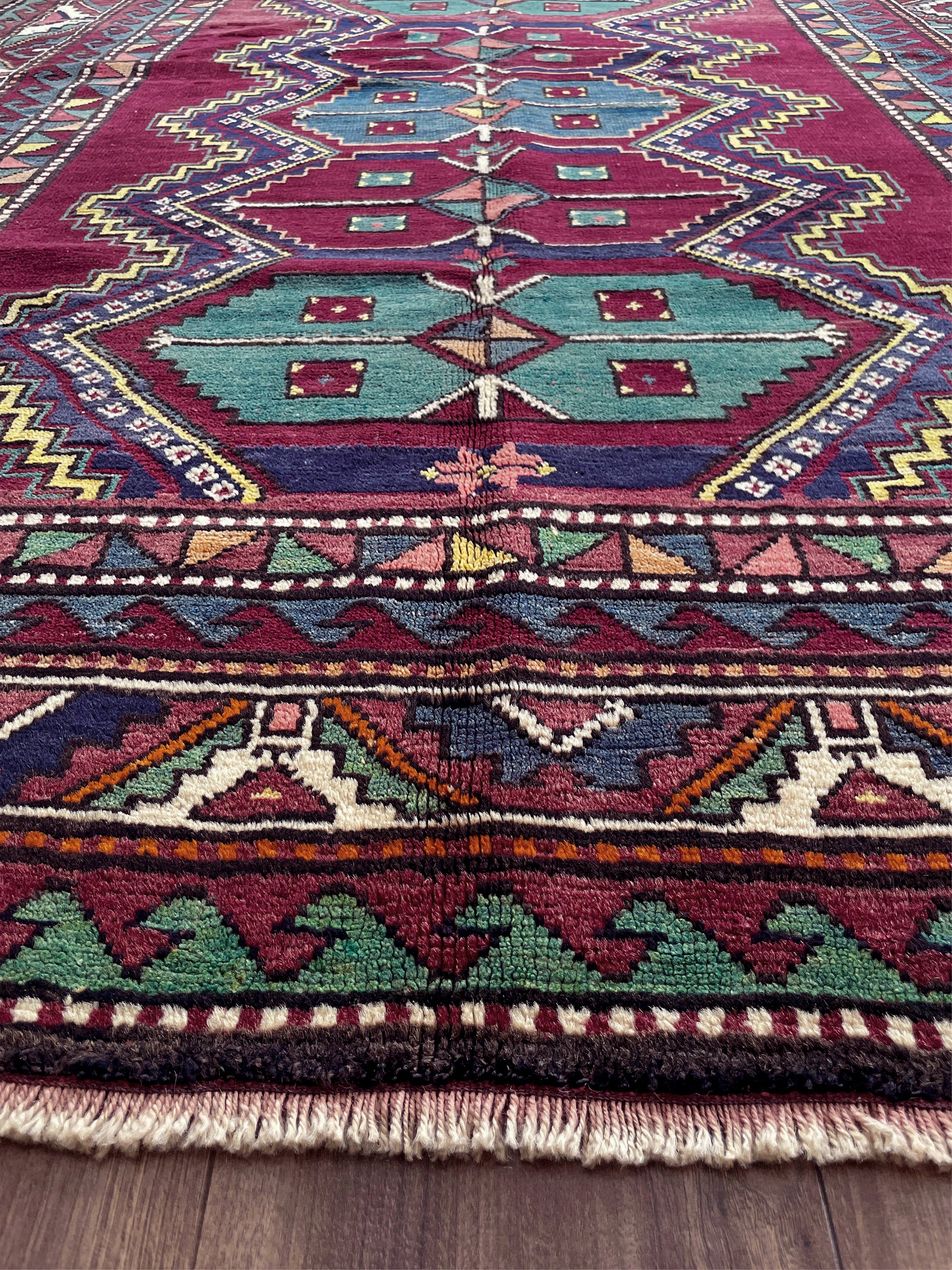 Close-up of a colorful patterned rug with geometric designs on a wooden floor. vintage kazak caucasian rug 6x9 burgundy field tribal geometric handmade wool 1940s antique style rug san francisco bay area rug shop indigo rugs